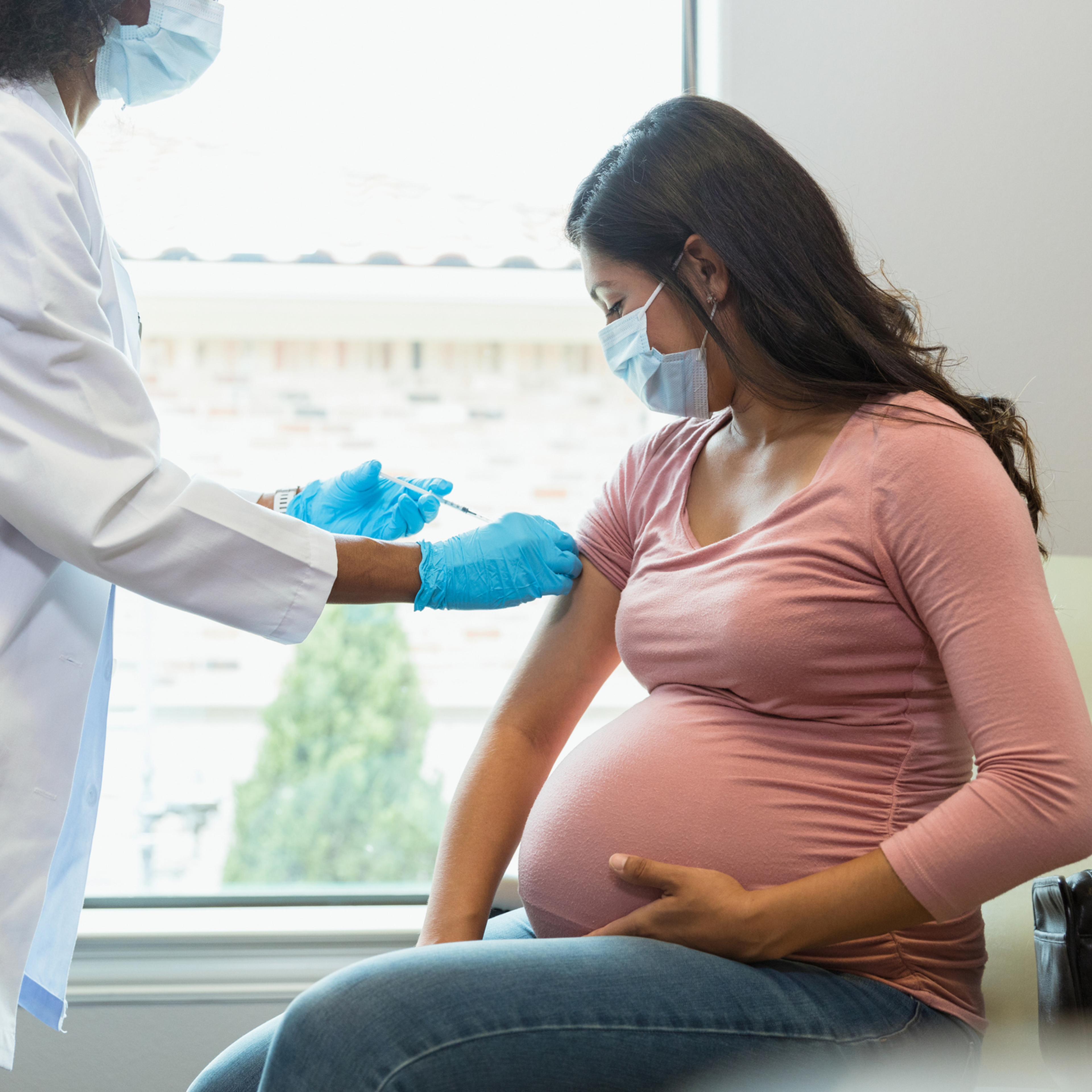 Expectant mother watches as tech gives her vaccine