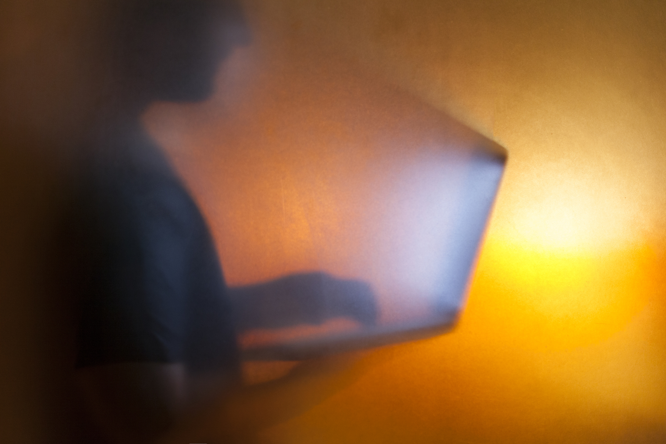 Man using laptop behind translucent glass with warm background