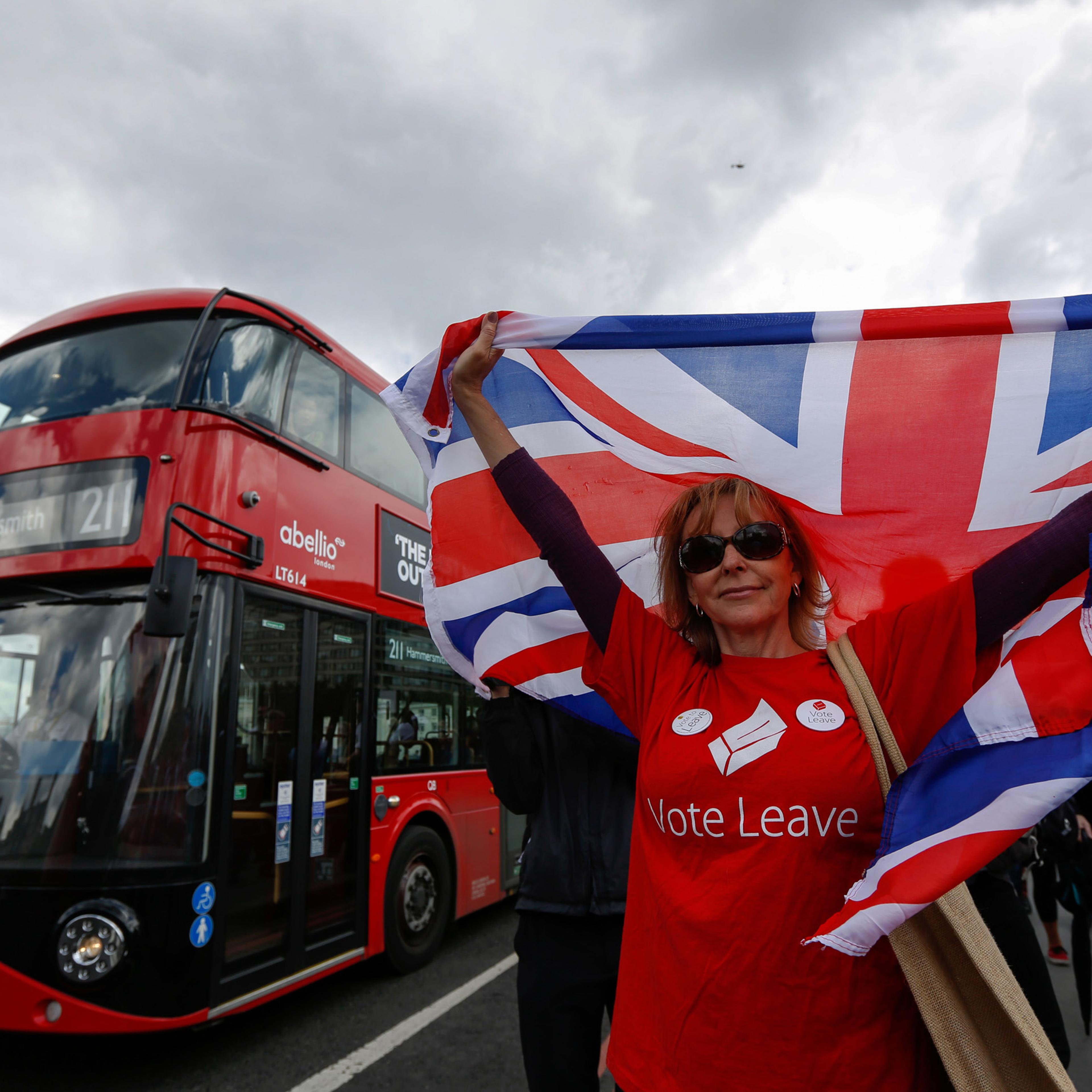 A campaigner wearing a Vote Leave t-shirt and holding a British Union Flag, also known as a Union Jack, stands on a Westminster Bridge near the Houses of Parliament in London on June 15, 2016.