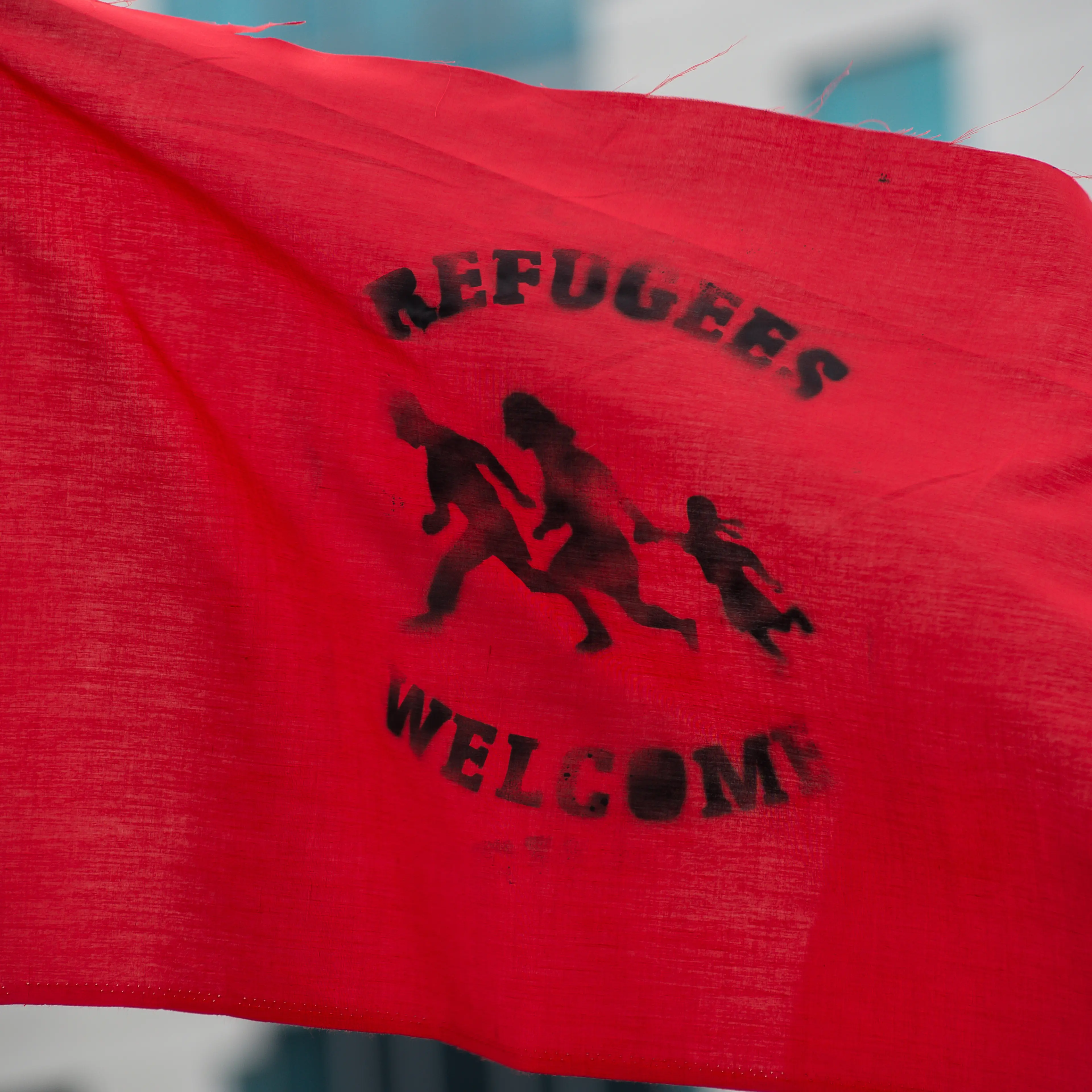 A demonstrator holds a flag declaring "Refugees Welcome." A