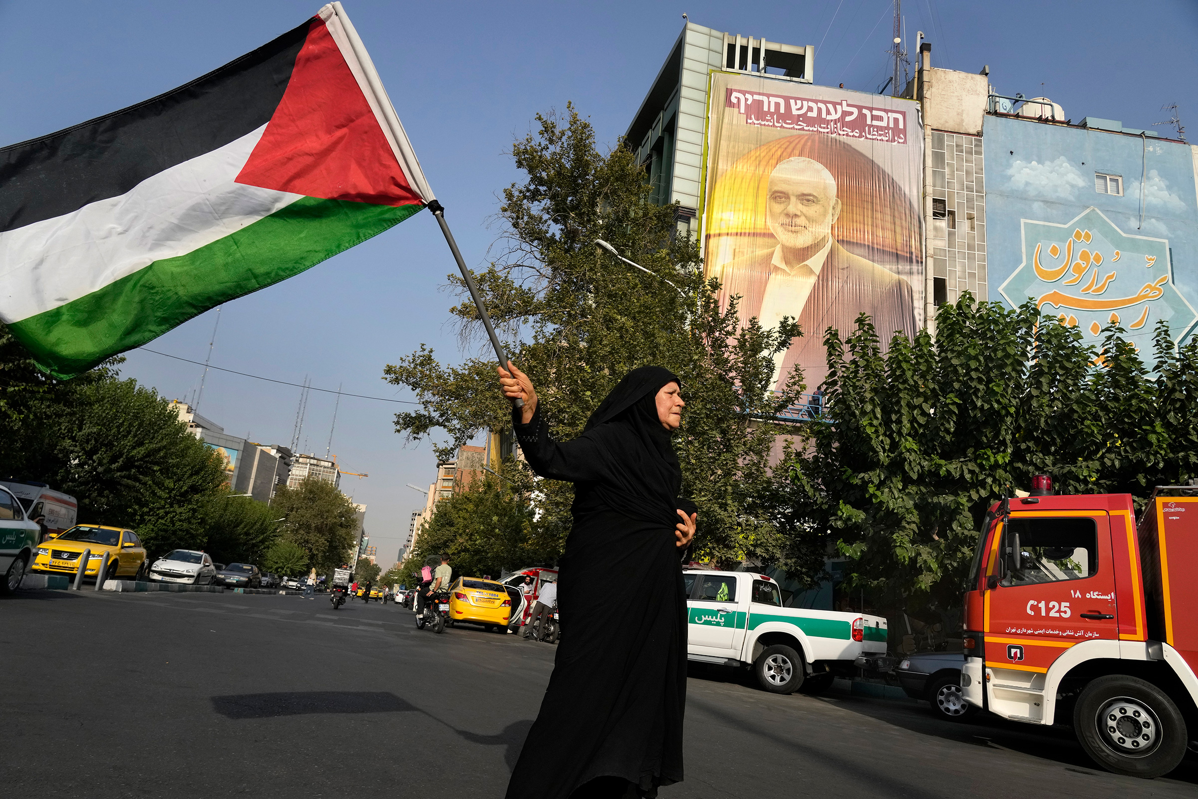 An Iranian woman waves a Palestinian flag prior to a demonstration to condemn the killing of Hamas leader Ismail Haniyeh, in front of a huge banner on a building showing his portrait with a sign which reads in Farsi and Hebrew: "Wait for severe punishmen