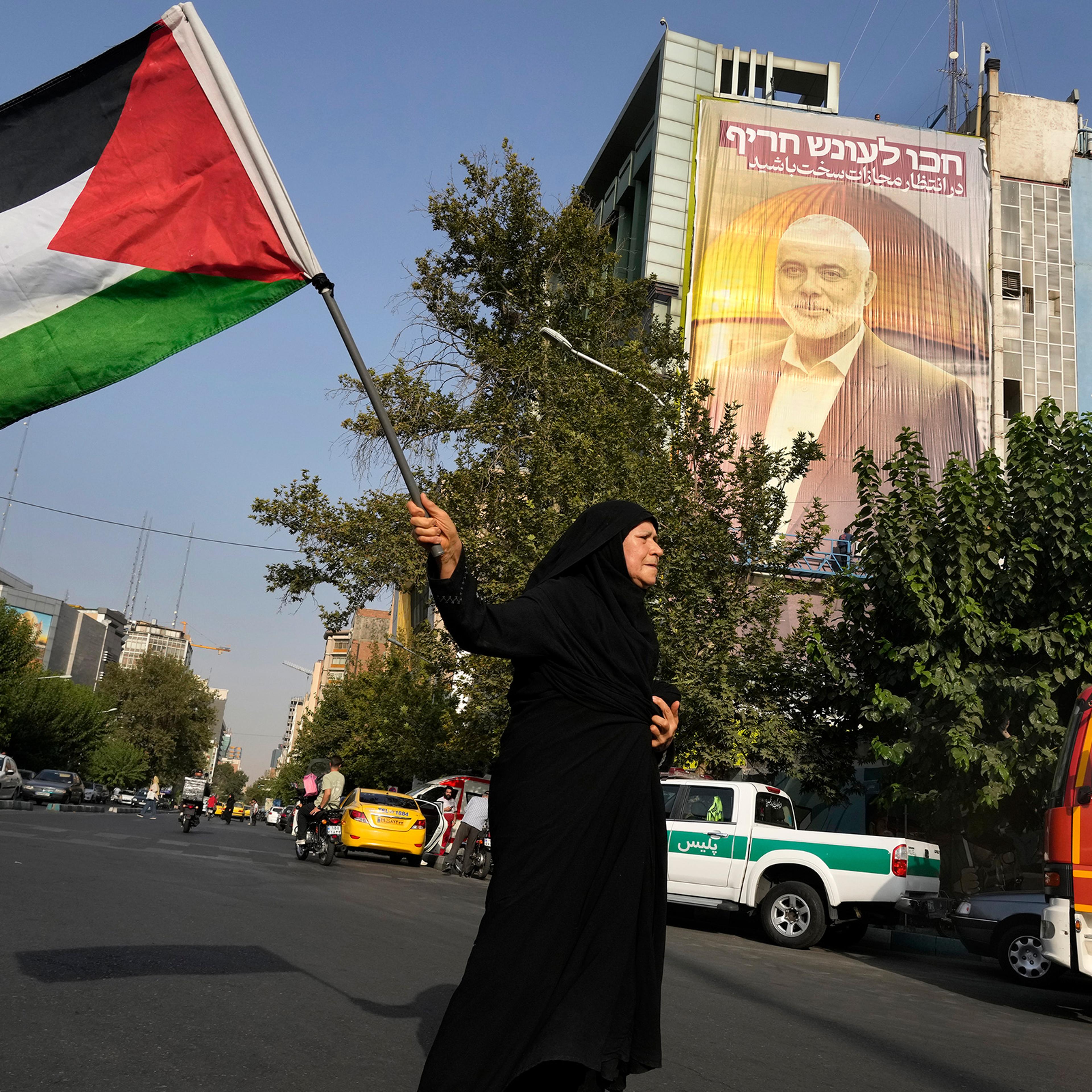An Iranian woman waves a Palestinian flag prior to a demonstration to condemn the killing of Hamas leader Ismail Haniyeh, in front of a huge banner on a building showing his portrait with a sign which reads in Farsi and Hebrew: "Wait for severe punishmen