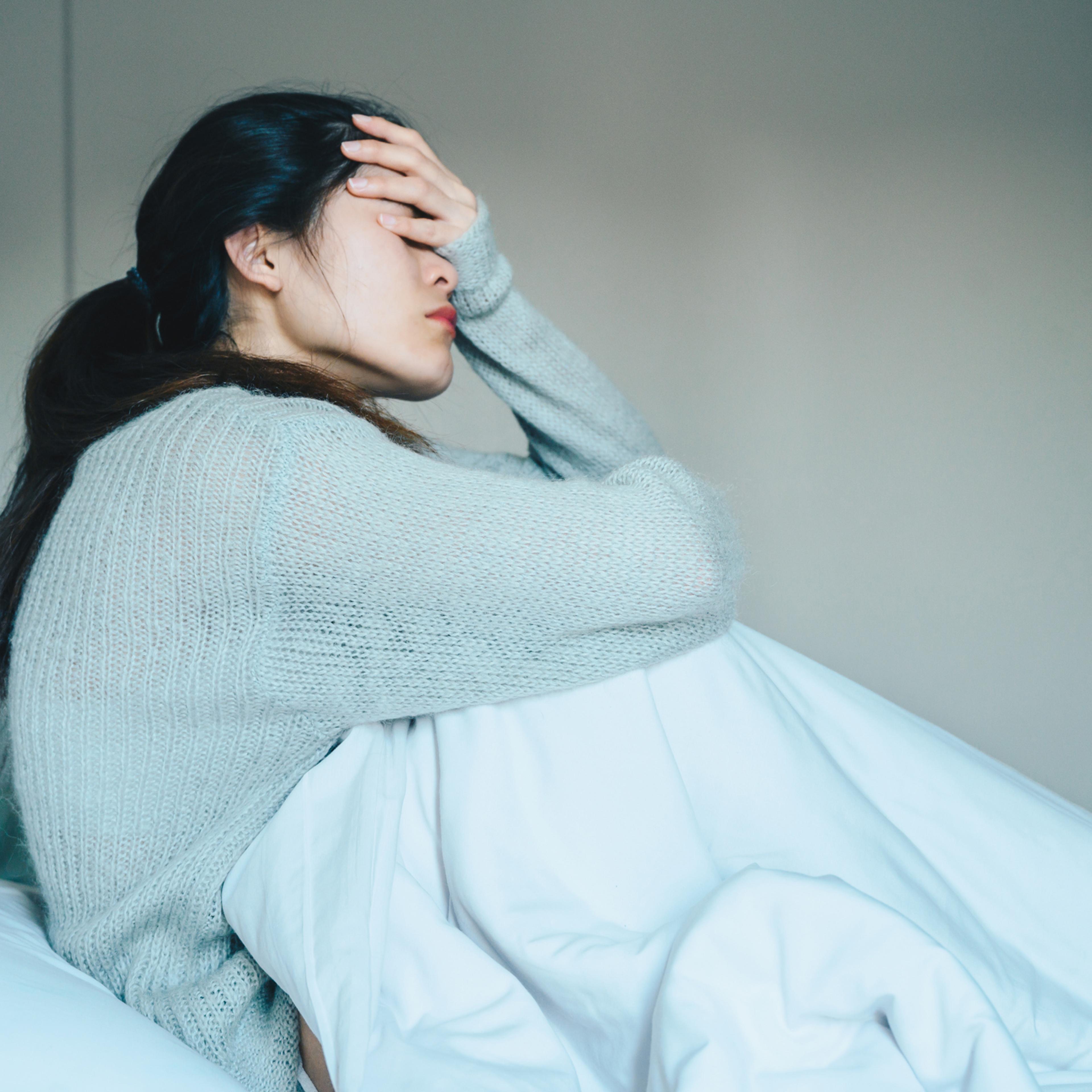 Portrait of sickness woman sitting alone on the bed in the bedroom, self isolation herself during coronavirus pandemic outbreak.