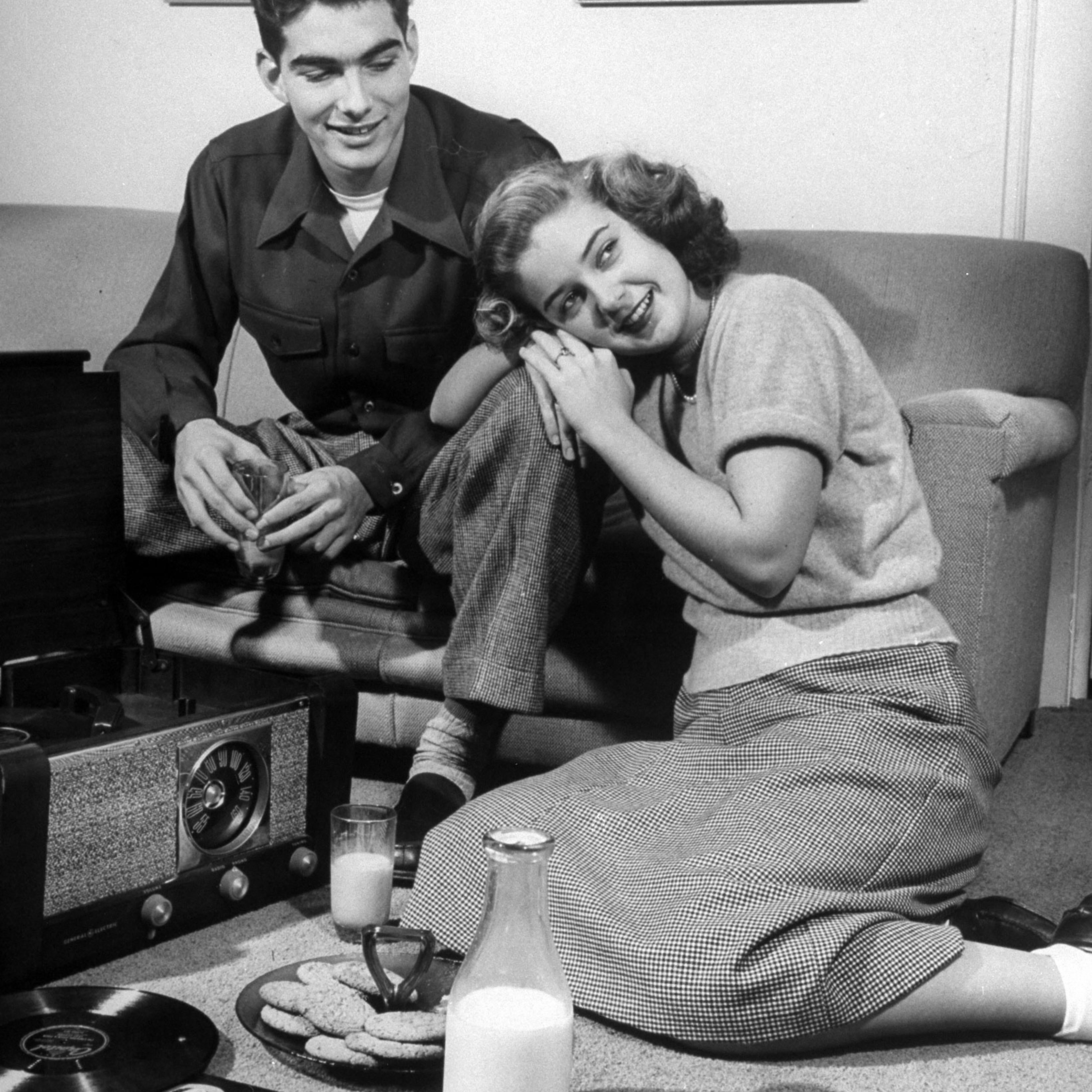 Teenage couple listening to records and having a snack of milk and cookies.
