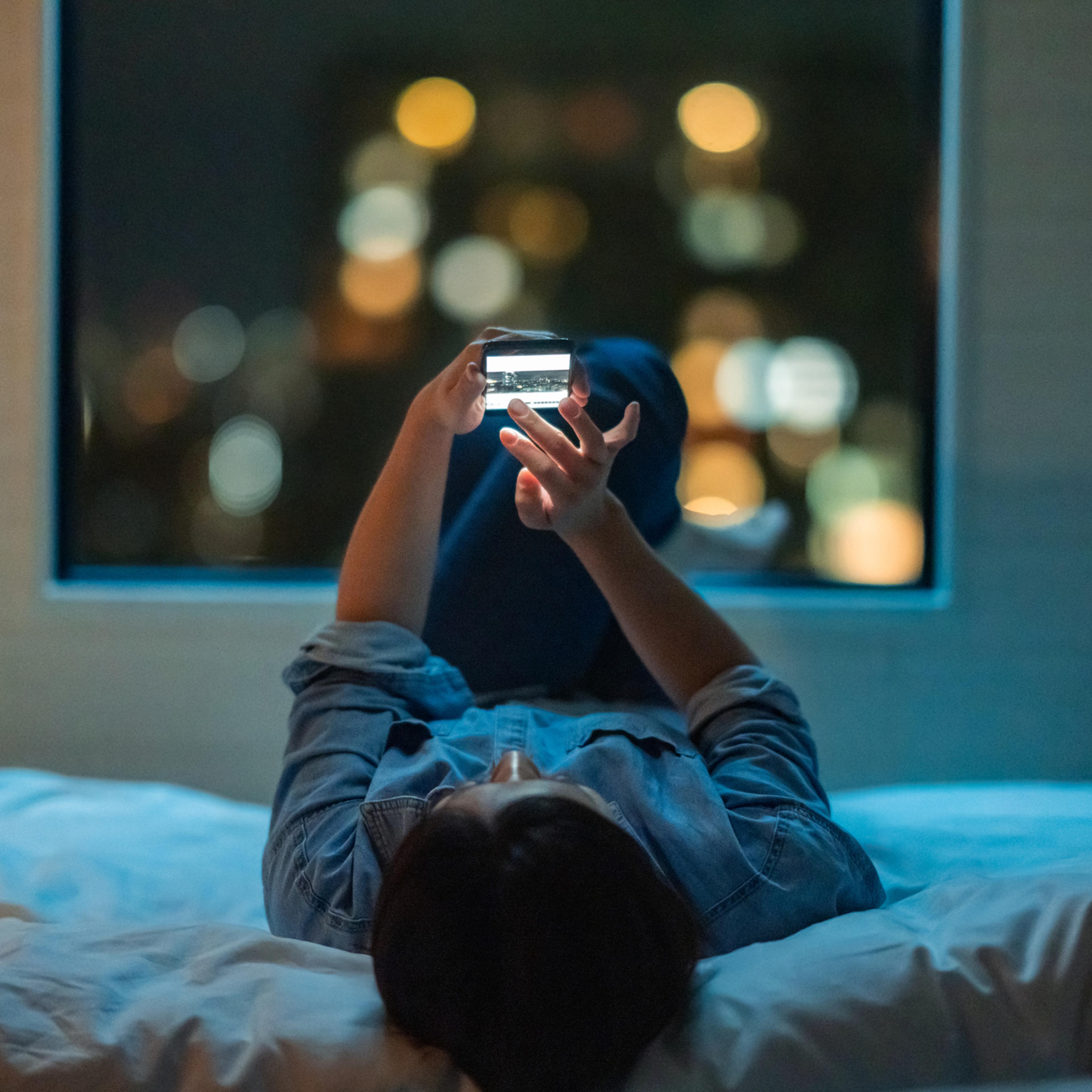 Woman lying down on bed and using smart phone at night