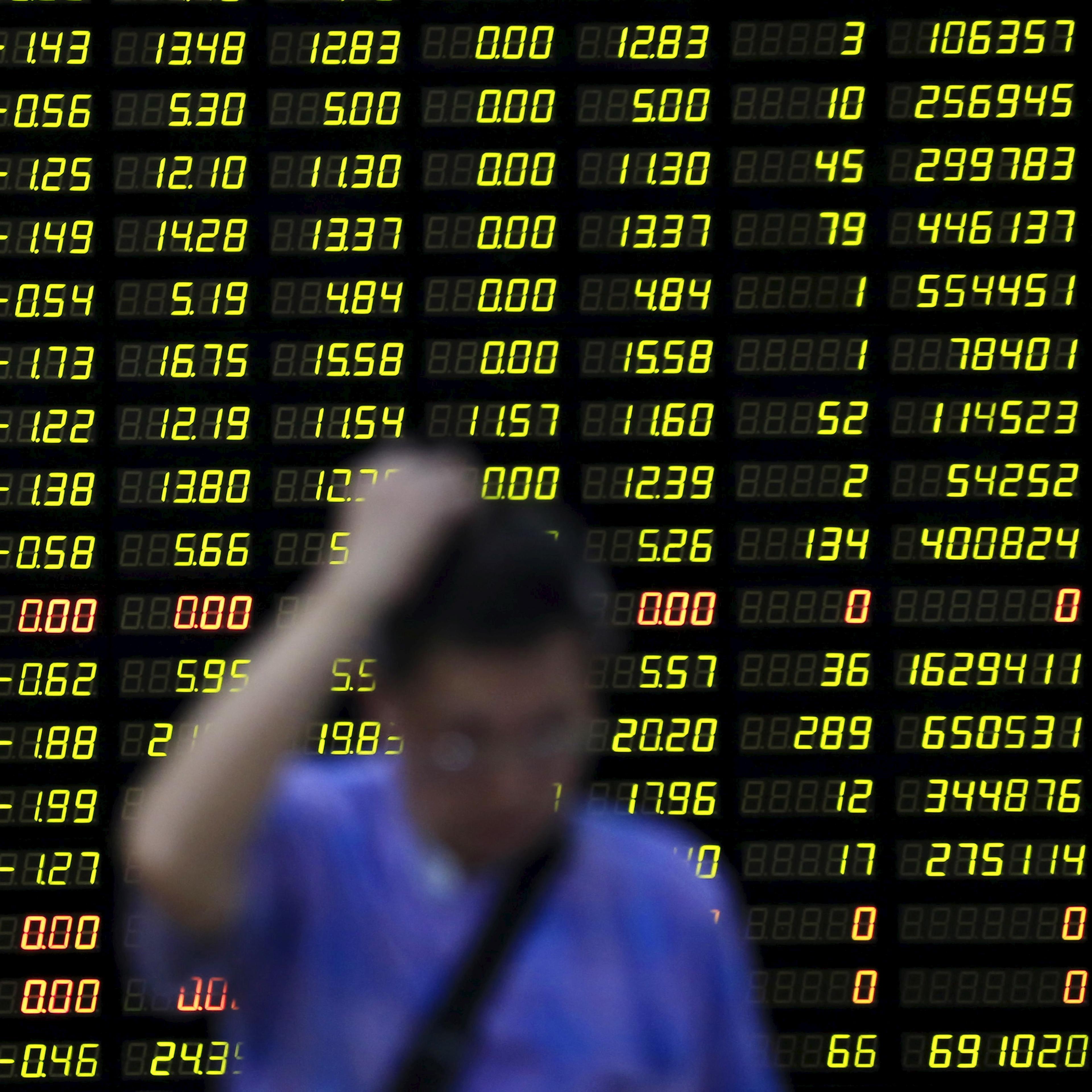 An investor stands in front of electronic board showing stock information at brokerage house in Shanghai