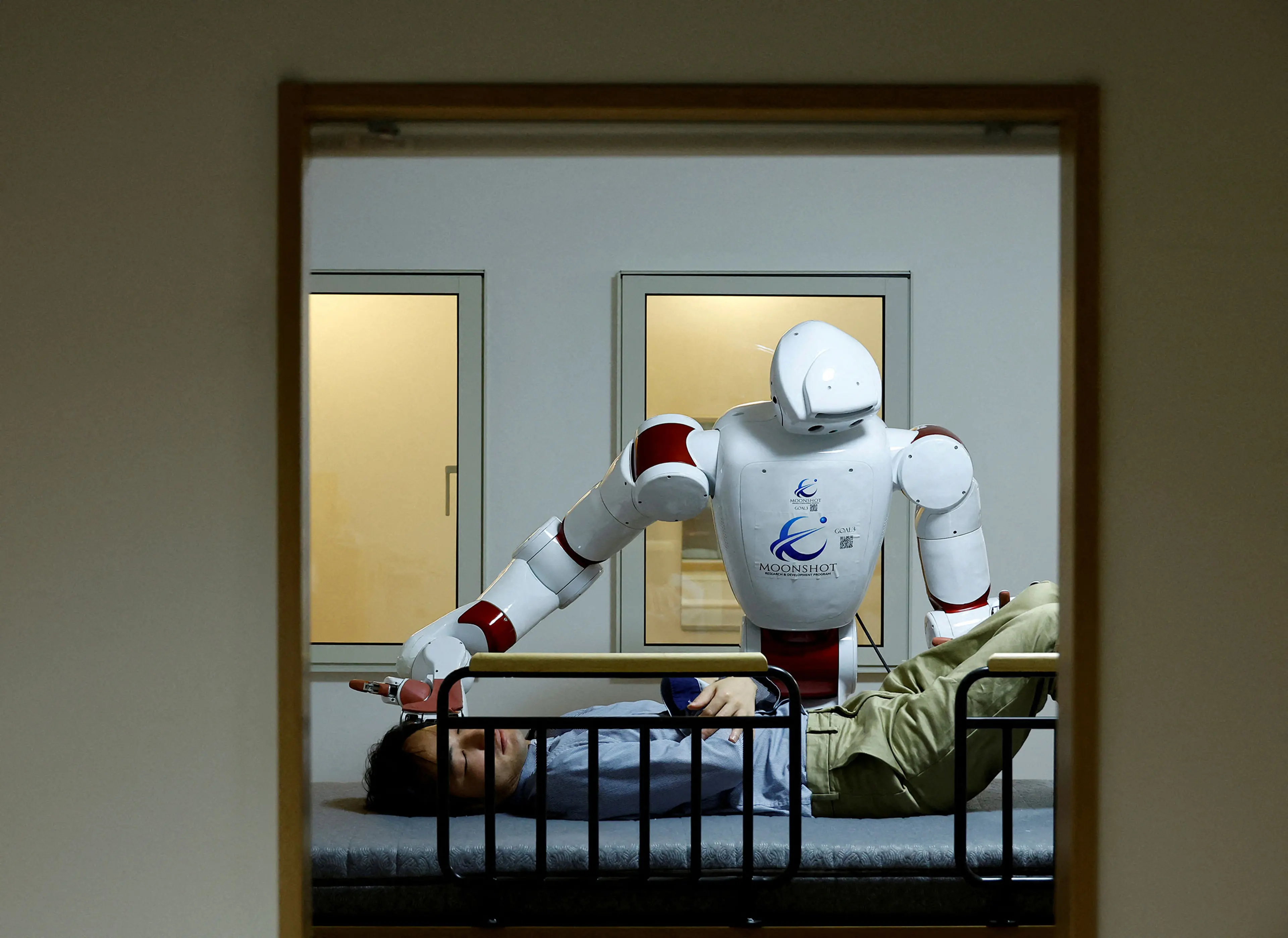 AIREC, an artificial intelligence (AI)-driven humanoid robot, demonstrates a manoeuvre for changing diapers or preventing bedsores with a researcher at Waseda University's laboratory in Tokyo
