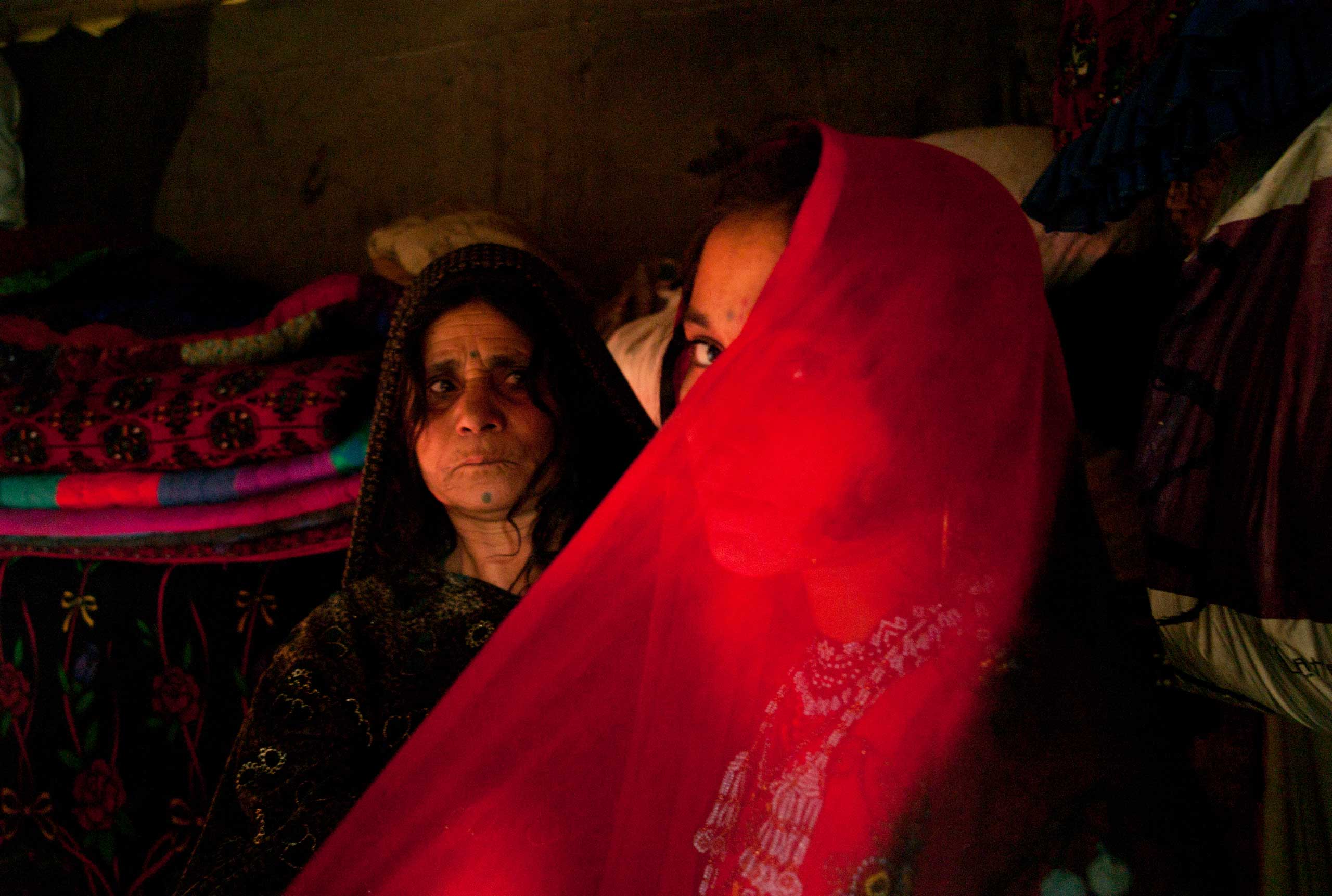 LAHORE, PAKISTAN- NOVEMBER 2009
A few days ahead of her wedding, 14 year old Afghan refugee Zeenat Gul is helped by her mother as she tries on her hand made red beaded wedding dress at their one room home in the slums of Sagiam Pull.
One of ten siblings, Zeenat was born at the refugee camp of Kohart in Pakistan's North West Frontier Province after her family fled fighting in Kunduz.
Zeenat Gul has yet to meet her fiance but has been busy making her in-laws to be gifts of beaded combs, mirrors and jewelry. Now liberated from her work in the dump, her mother Barangul has been advising her teenage daughter about marriage. The sensitive topic of sex will not be raised until the wedding night, "When a girl marries, then she will become a woman".