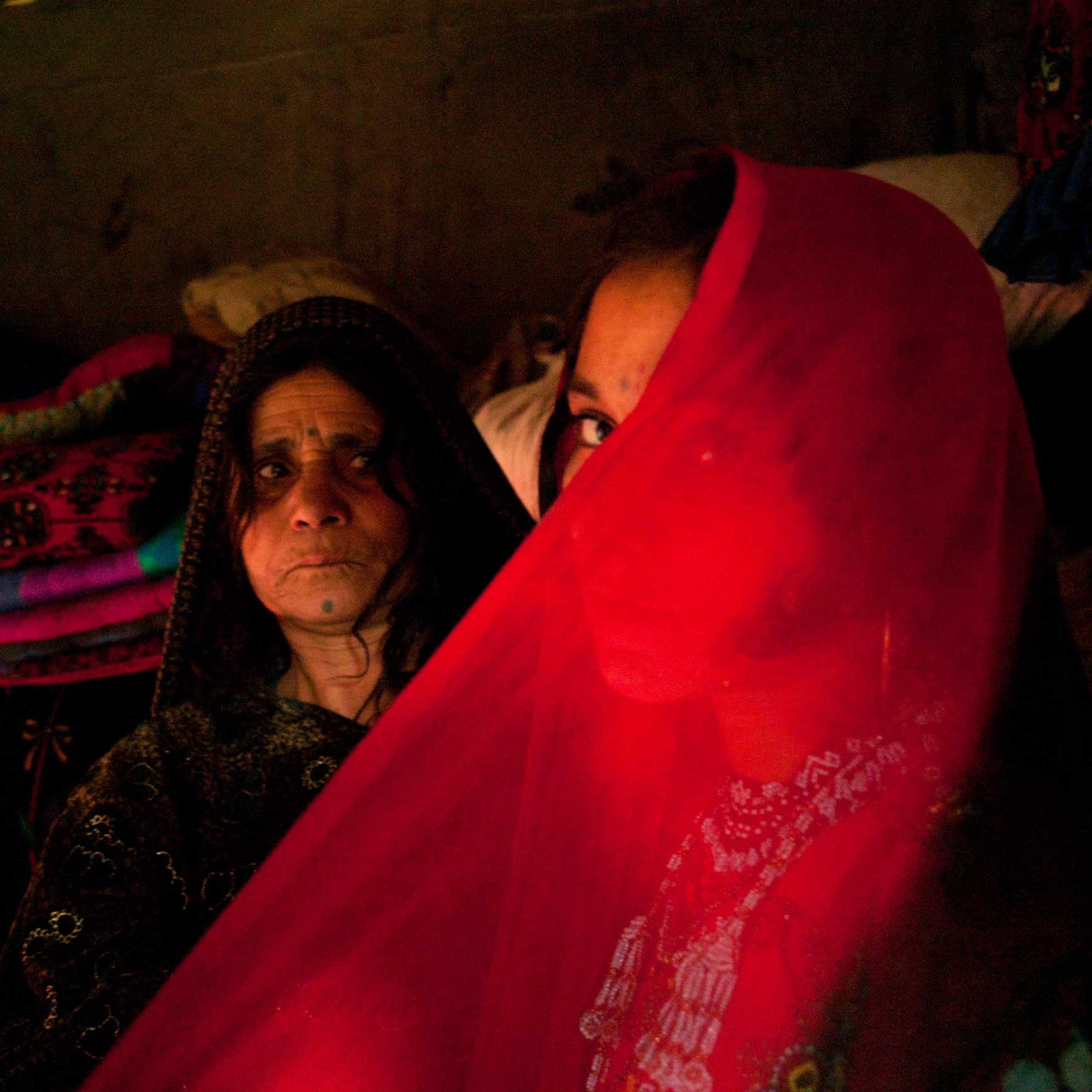LAHORE, PAKISTAN- NOVEMBER 2009
A few days ahead of her wedding, 14 year old Afghan refugee Zeenat Gul is helped by her mother as she tries on her hand made red beaded wedding dress at their one room home in the slums of Sagiam Pull.
One of ten siblings, Zeenat was born at the refugee camp of Kohart in Pakistan's North West Frontier Province after her family fled fighting in Kunduz.
Zeenat Gul has yet to meet her fiance but has been busy making her in-laws to be gifts of beaded combs, mirrors and jewelry. Now liberated from her work in the dump, her mother Barangul has been advising her teenage daughter about marriage. The sensitive topic of sex will not be raised until the wedding night, "When a girl marries, then she will become a woman".