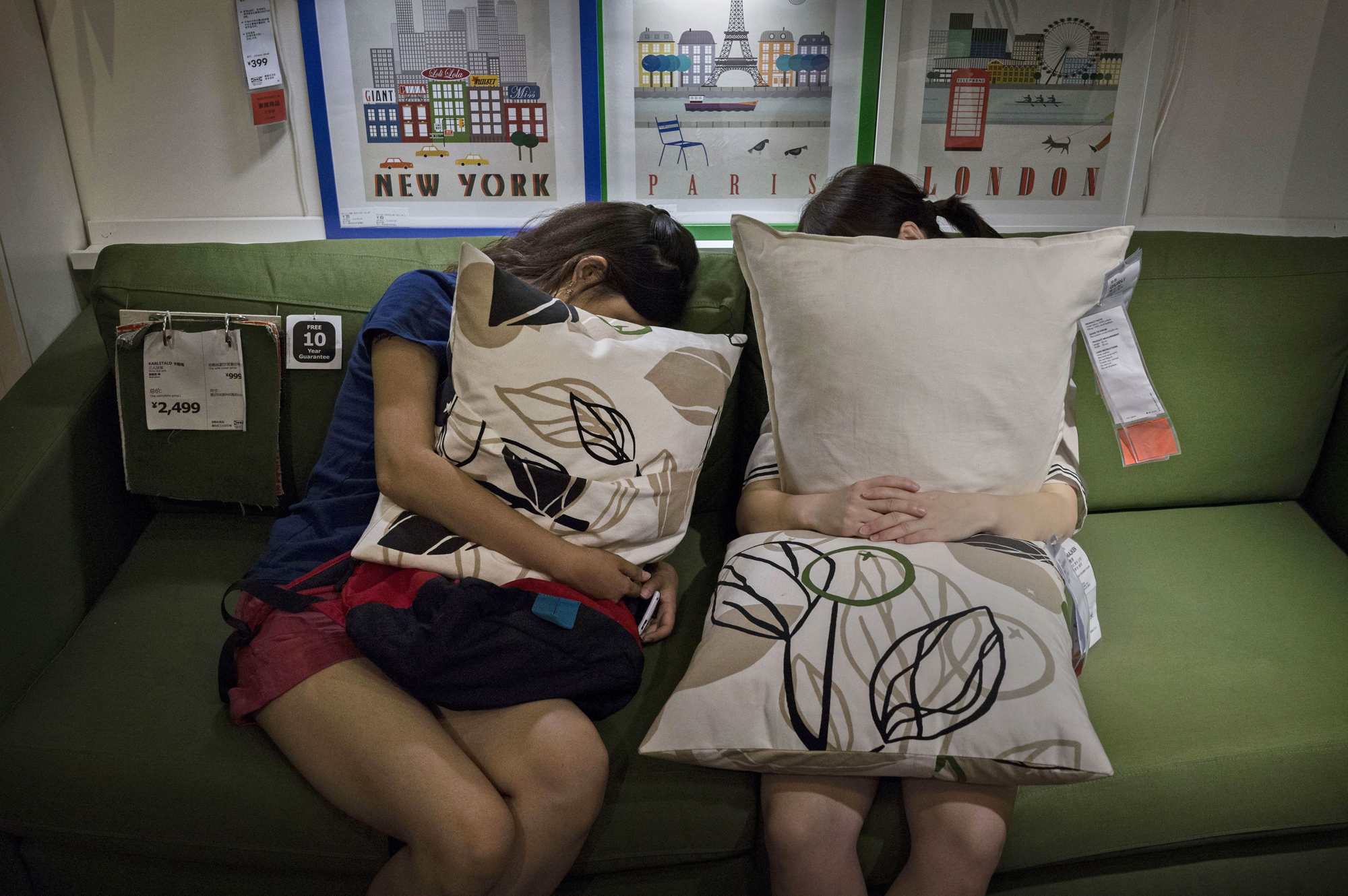 Shoppers clutch pillows as they sleep on a sofa in the showroom of the IKEA store on July 6, 2014 in Beijing.