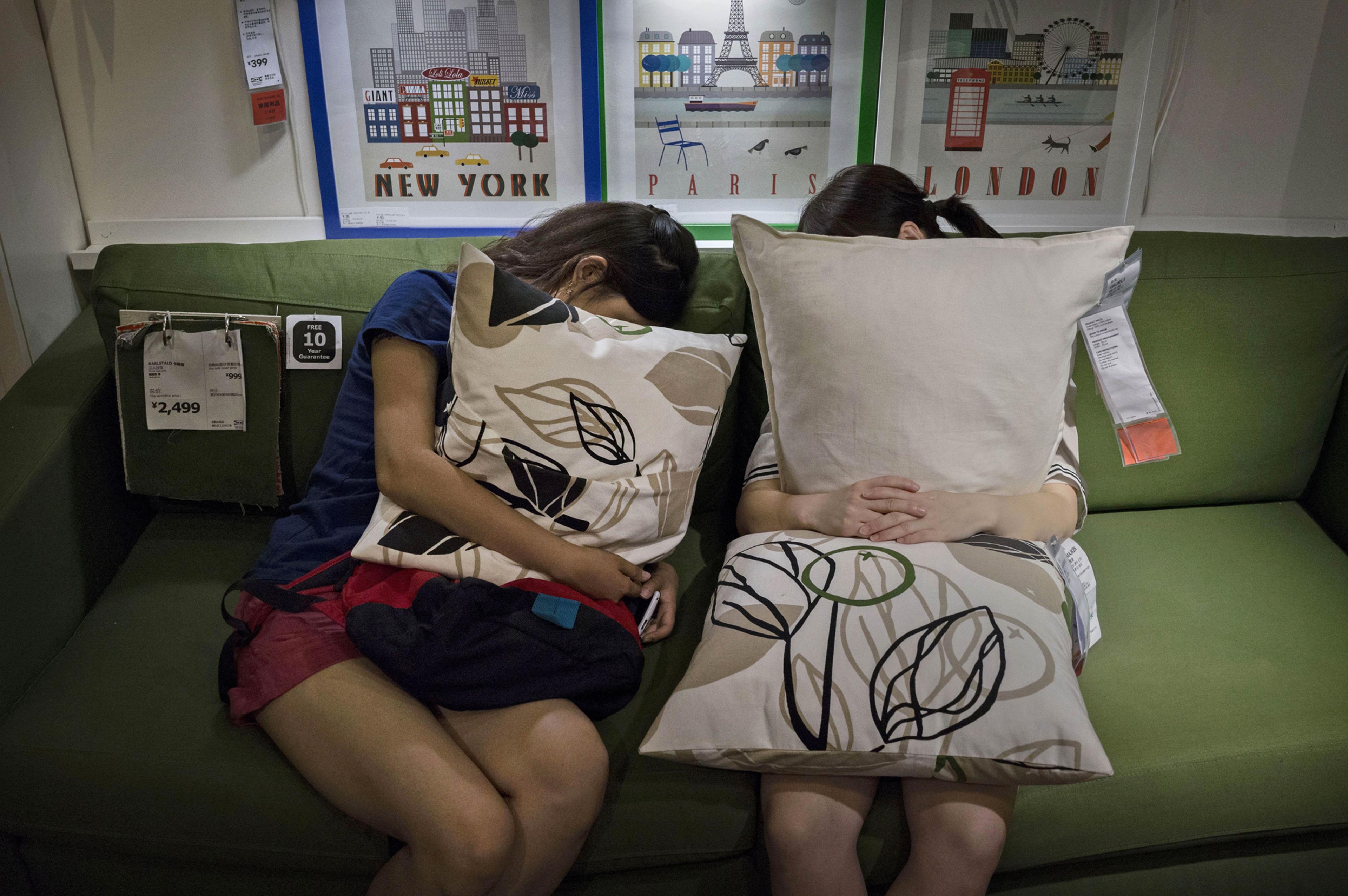 Shoppers clutch pillows as they sleep on a sofa in the showroom of the IKEA store on July 6, 2014 in Beijing.