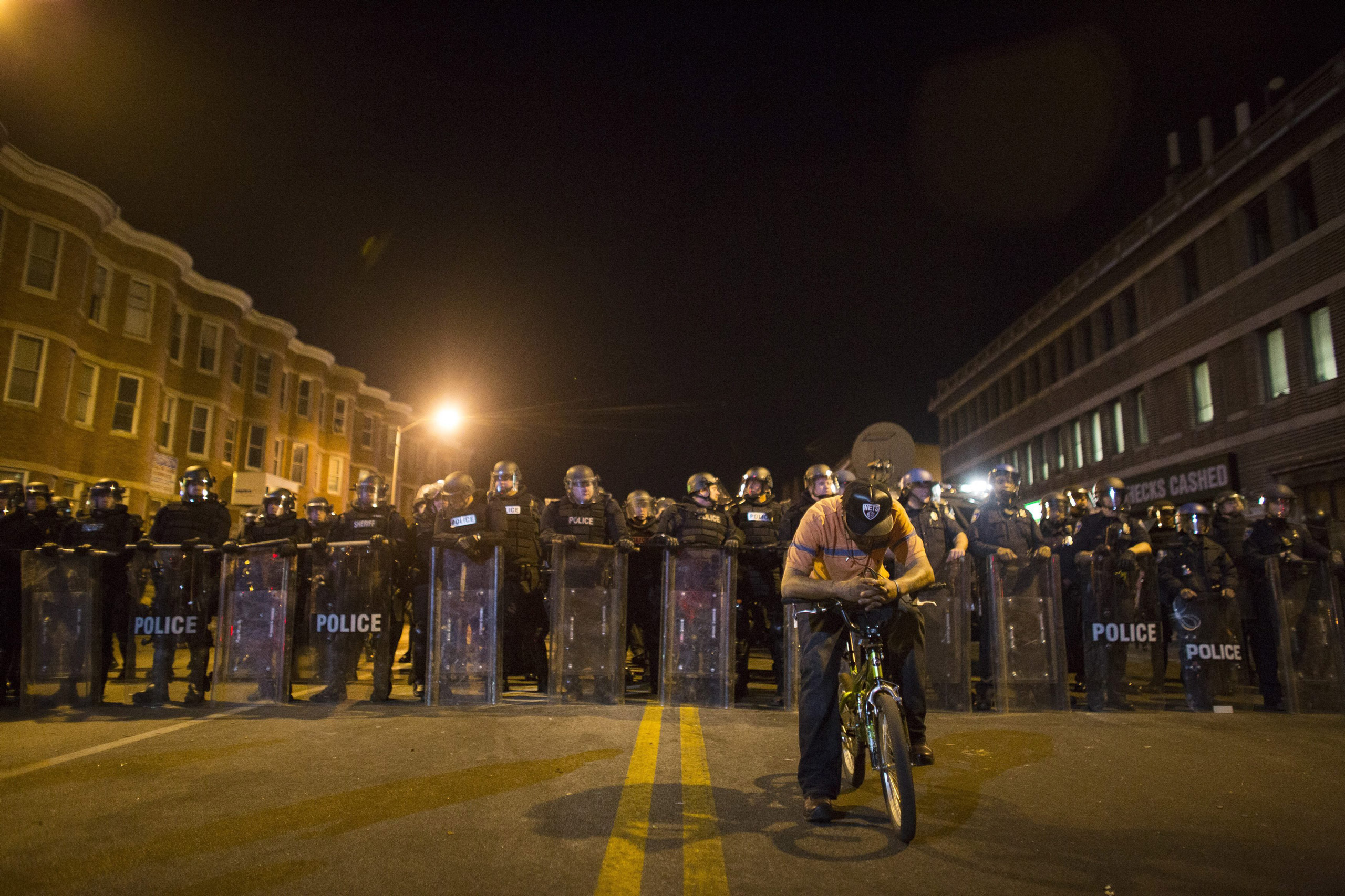 epa04988256 YEARENDER 2015 APRIL A protester on his bike is seen in front of a line of policemen in riot gear during a 10 p.m. curfew in Baltimore, Maryland, USA, 28 April 2015. Tensions eased on 28 April after peace-keeping civilians kept rock-throwing 