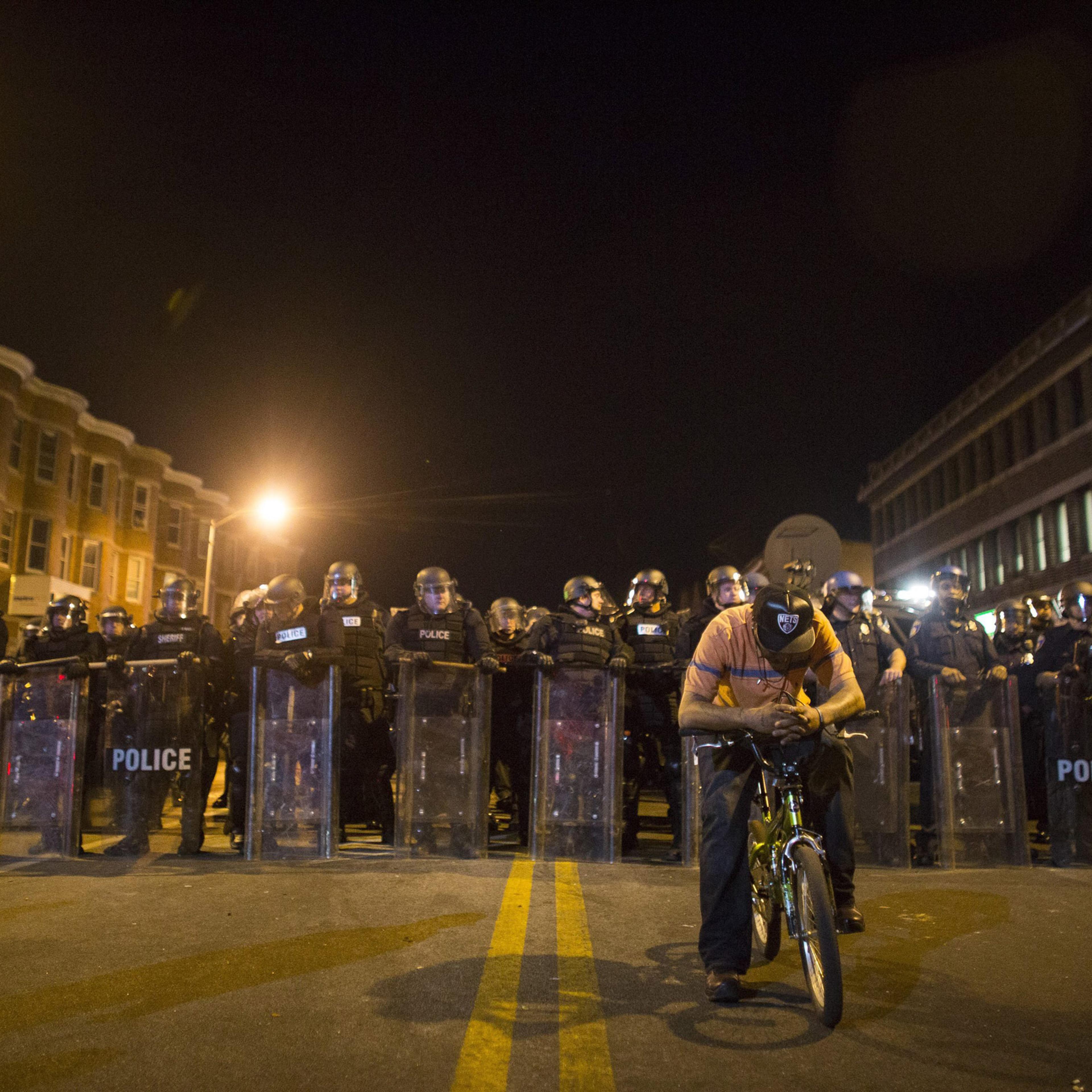 epa04988256 YEARENDER 2015 APRIL A protester on his bike is seen in front of a line of policemen in riot gear during a 10 p.m. curfew in Baltimore, Maryland, USA, 28 April 2015. Tensions eased on 28 April after peace-keeping civilians kept rock-throwing