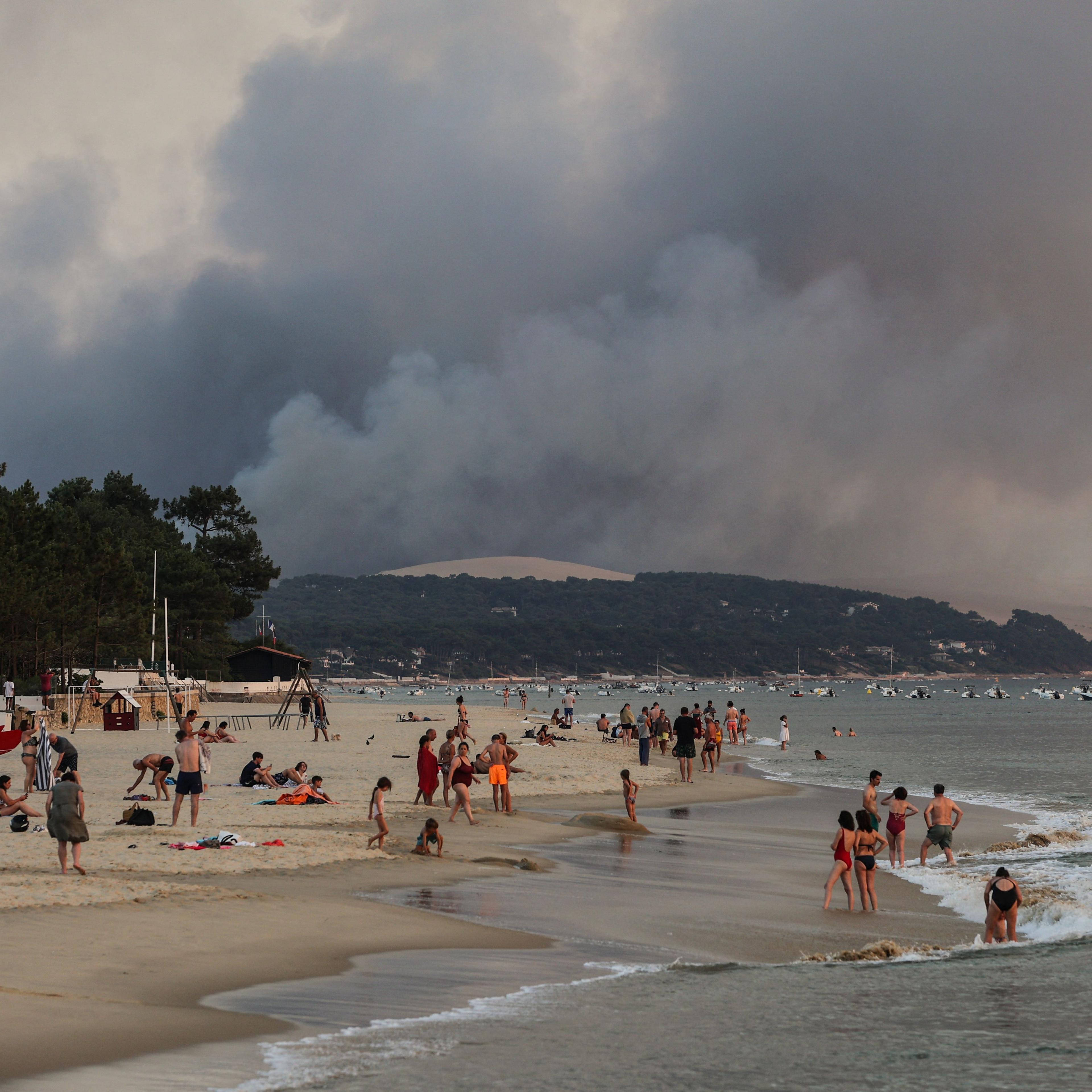 Smoke rises from a forest fire behind beachgoers in Arcachon, France, on July 18, 2022, when temperatures topped 100° F.