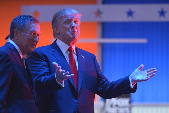 Real estate tycoon Donald Trump (R) confers with Ohio Governor John Kasich (L) during a break in the Republican presidential primary debate on August 6, 2015 at the Quicken Loans Arena in Cleveland, Ohio.