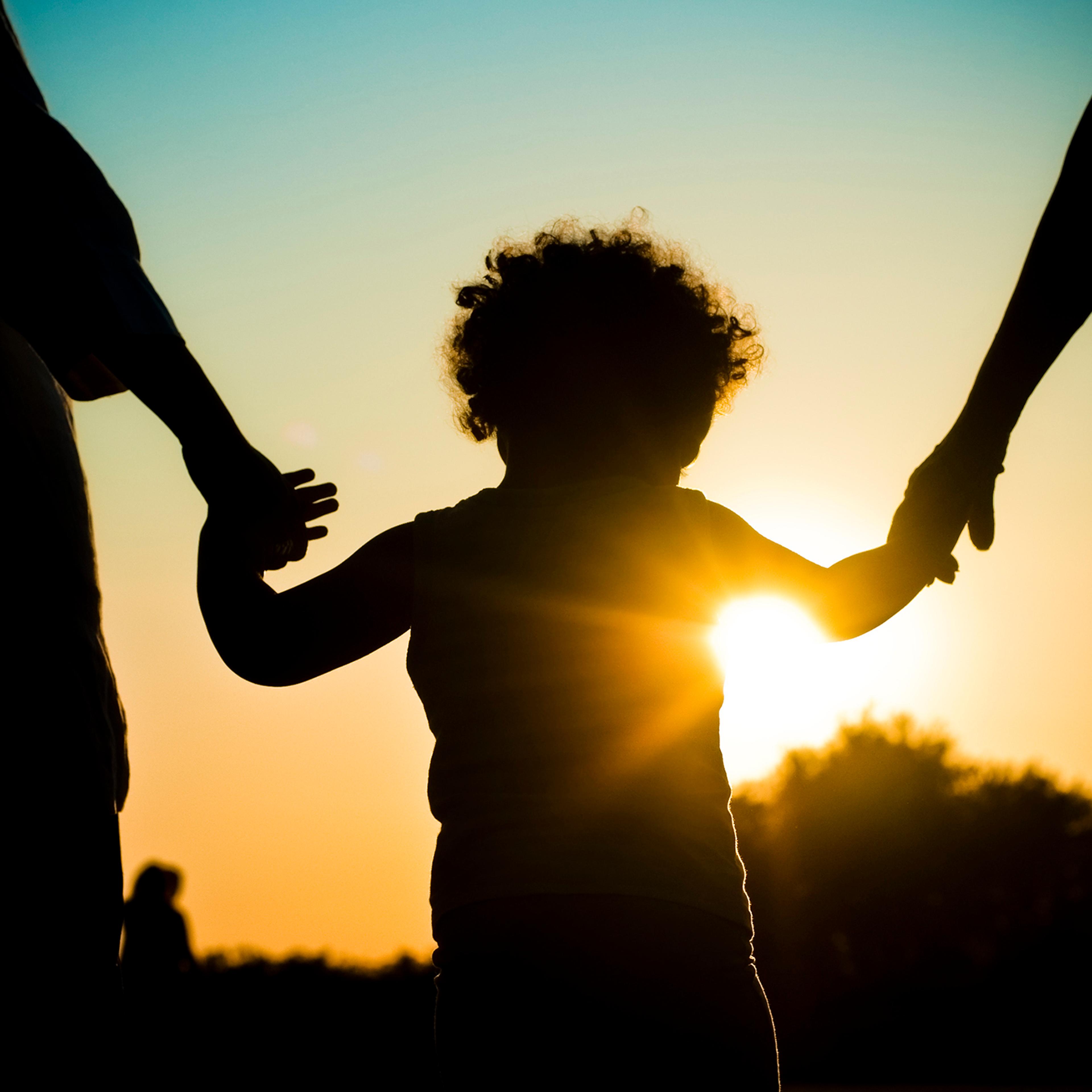 Silhouette of child holding hands with parents