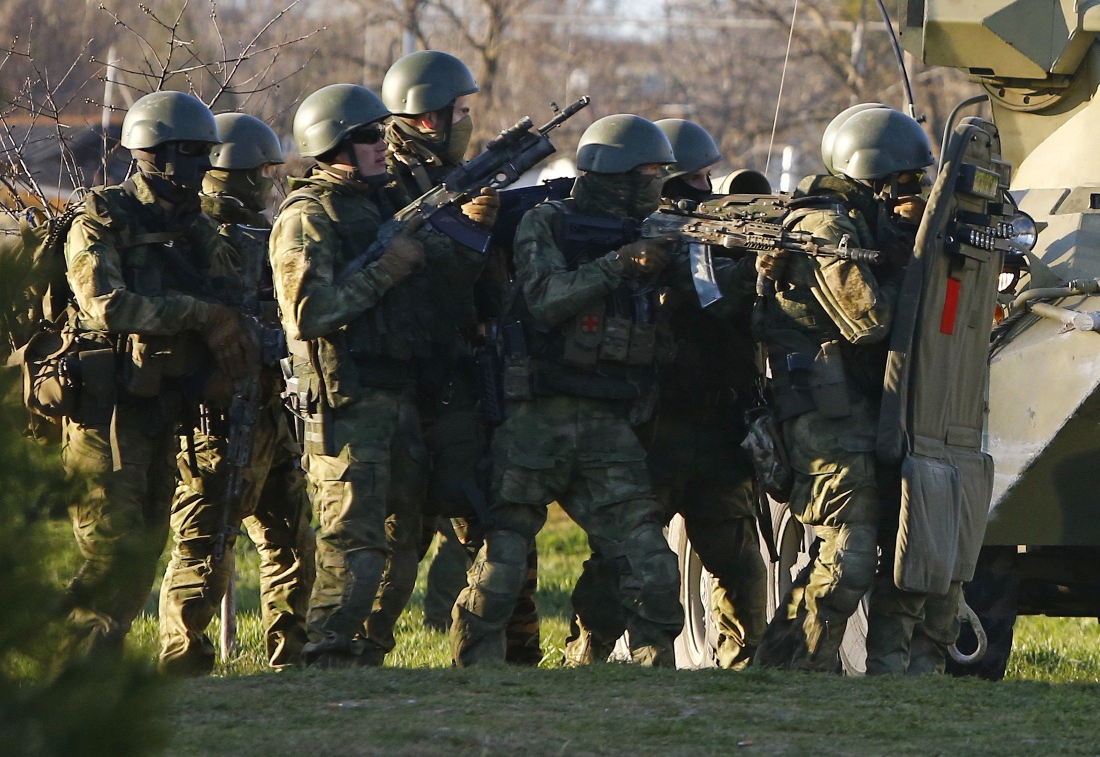 Armed men, believed to be Russian servicemen, take cover behind an armored vehicle as they attempt to take over a military airbase in the Crimean town of Belbek near Sevastopol, March 22, 2014.