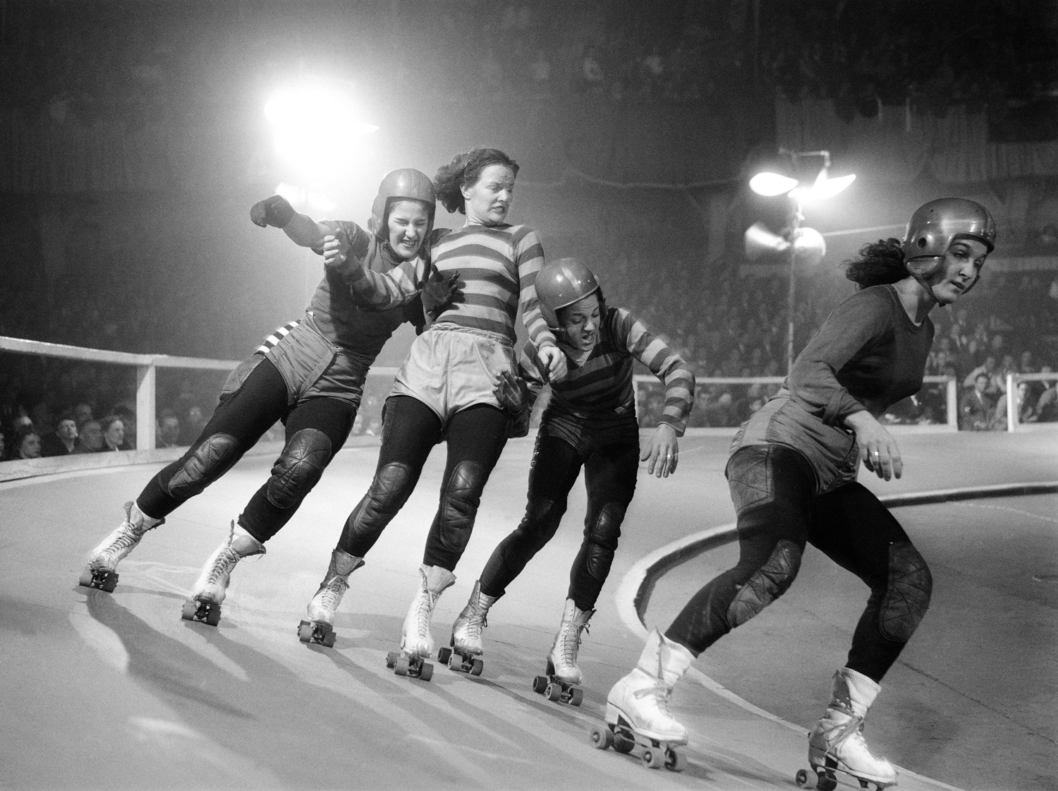 A skillful shoulder block thrown by 'Fuzzy' Buchek (left) foils an attempt by Vivian Johnson (center) to slip between two skaters and start a jam. Blocking and checking are both legal tactics under Derby rules.