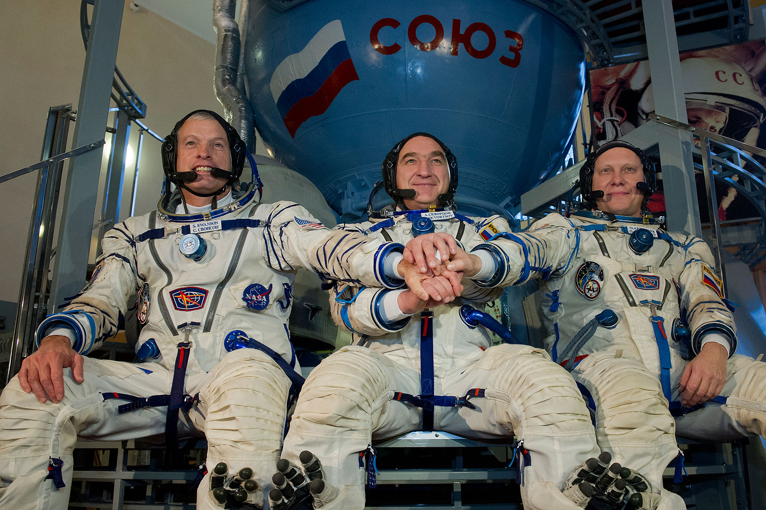 U.S. NASA astronaut Steven Swanson (L) joins hands with Russian cosmonauts, Alexander Skvortsov (C) and Oleg Artemyev (R), in front of a mock-up of a Soyuz TMA spacecraft at the Gagarin Cosmonauts' Training Centre in Star City centre outside Moscow, on March 5, 2014