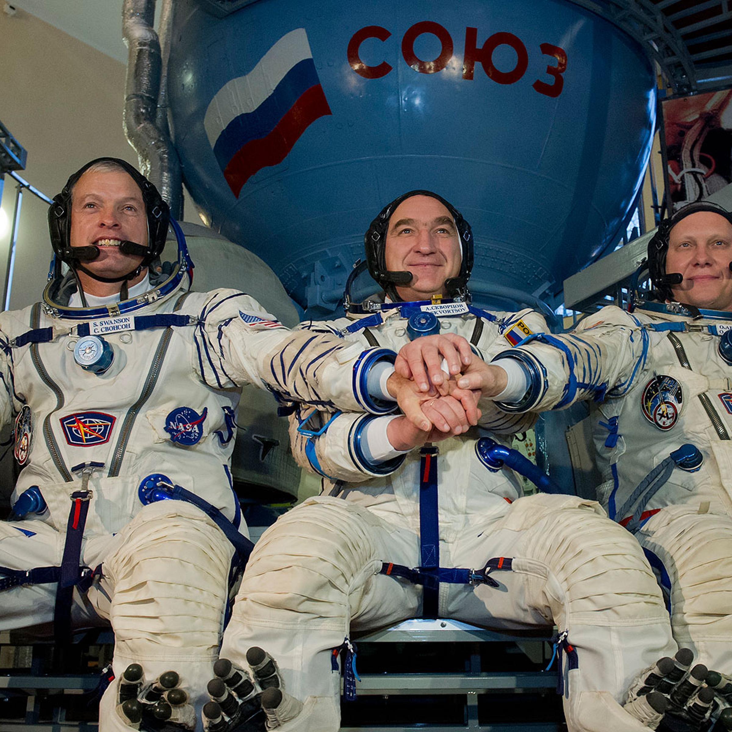 U.S. NASA astronaut Steven Swanson (L) joins hands with Russian cosmonauts, Alexander Skvortsov (C) and Oleg Artemyev (R), in front of a mock-up of a Soyuz TMA spacecraft at the Gagarin Cosmonauts' Training Centre in Star City centre outside Moscow, on March 5, 2014