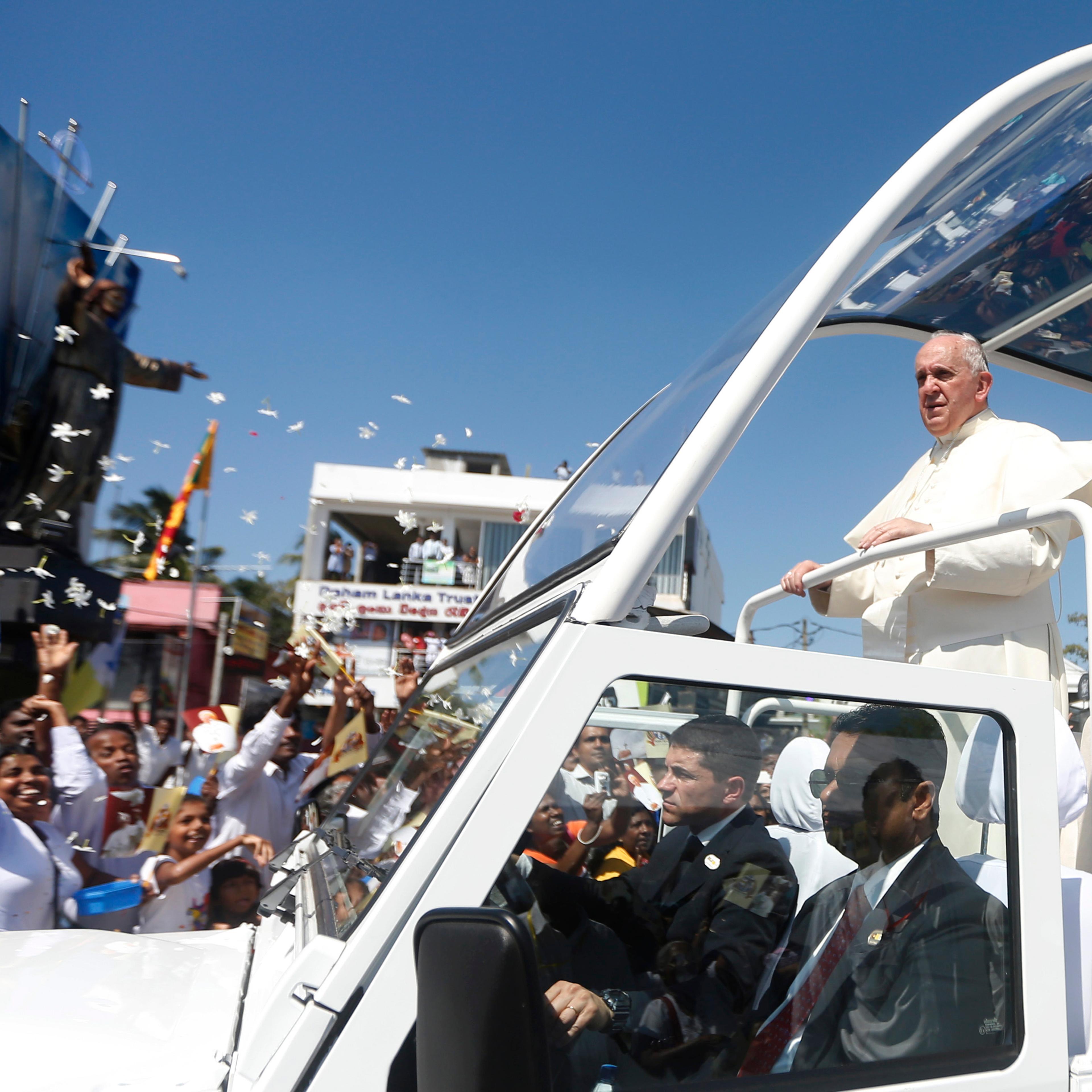 Pope Francis stands on his vehicle as devotees gather on the road to see him after he arrived at the Colombo airport