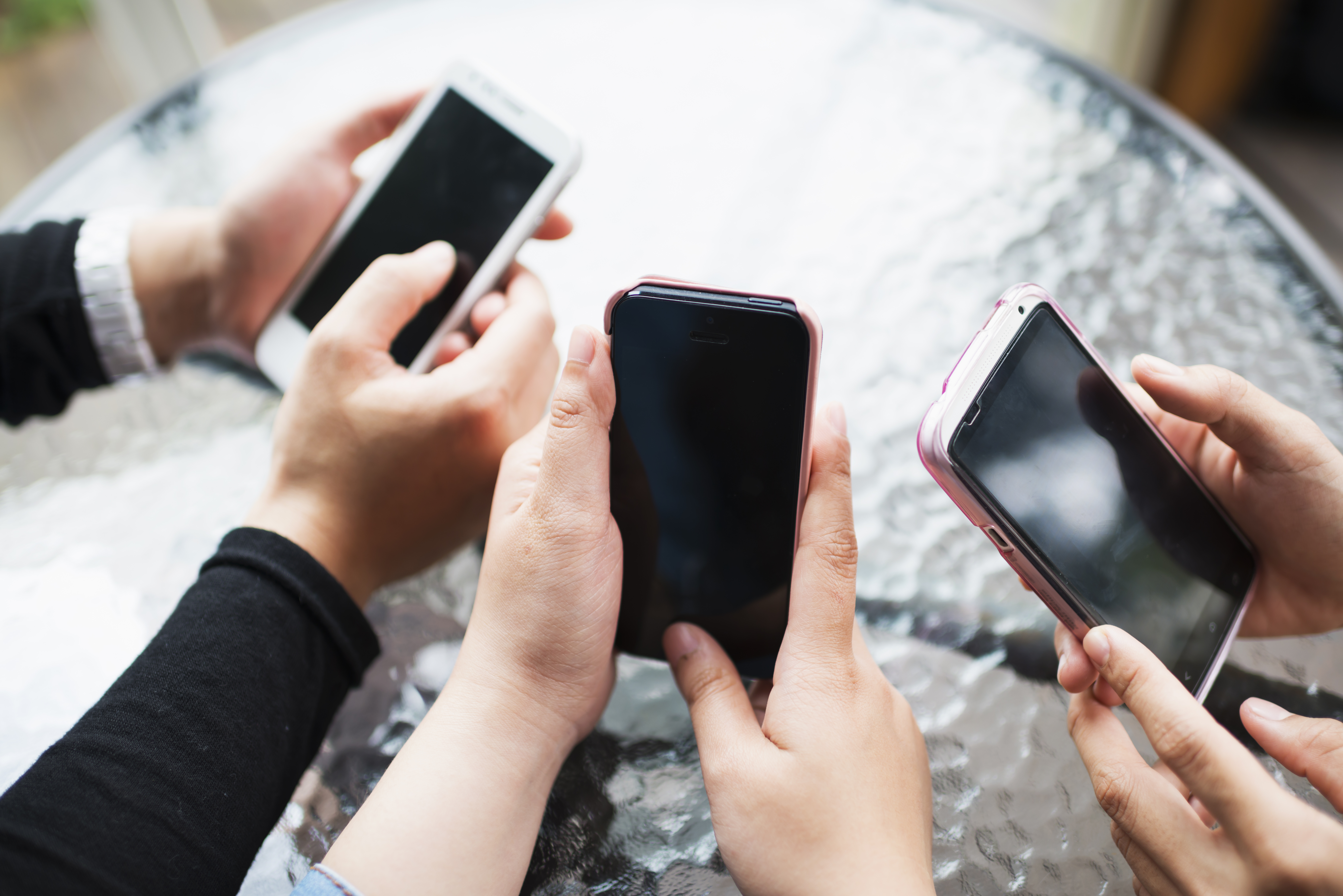 Three girls hold and use smart phones