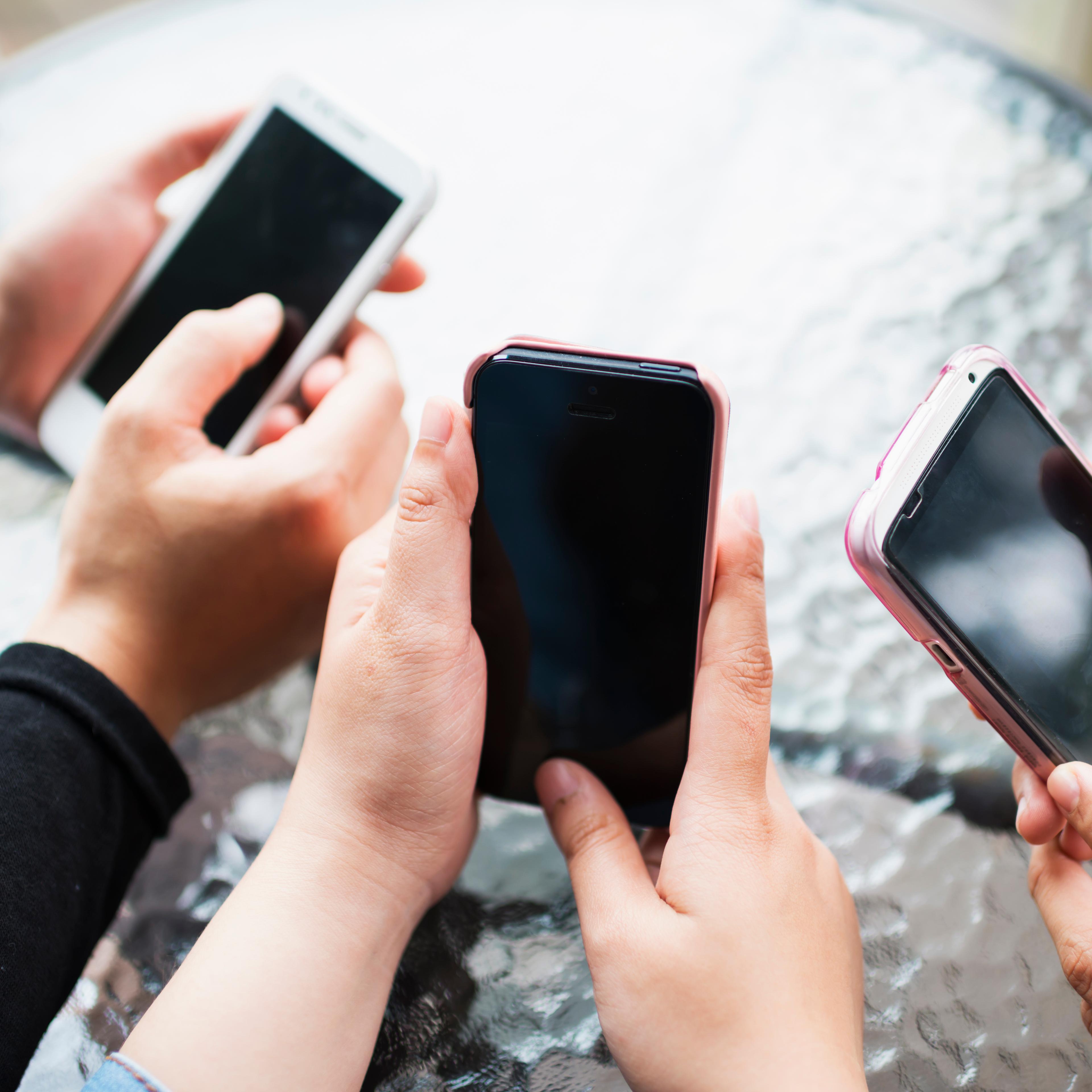 Three girls hold and use smart phones