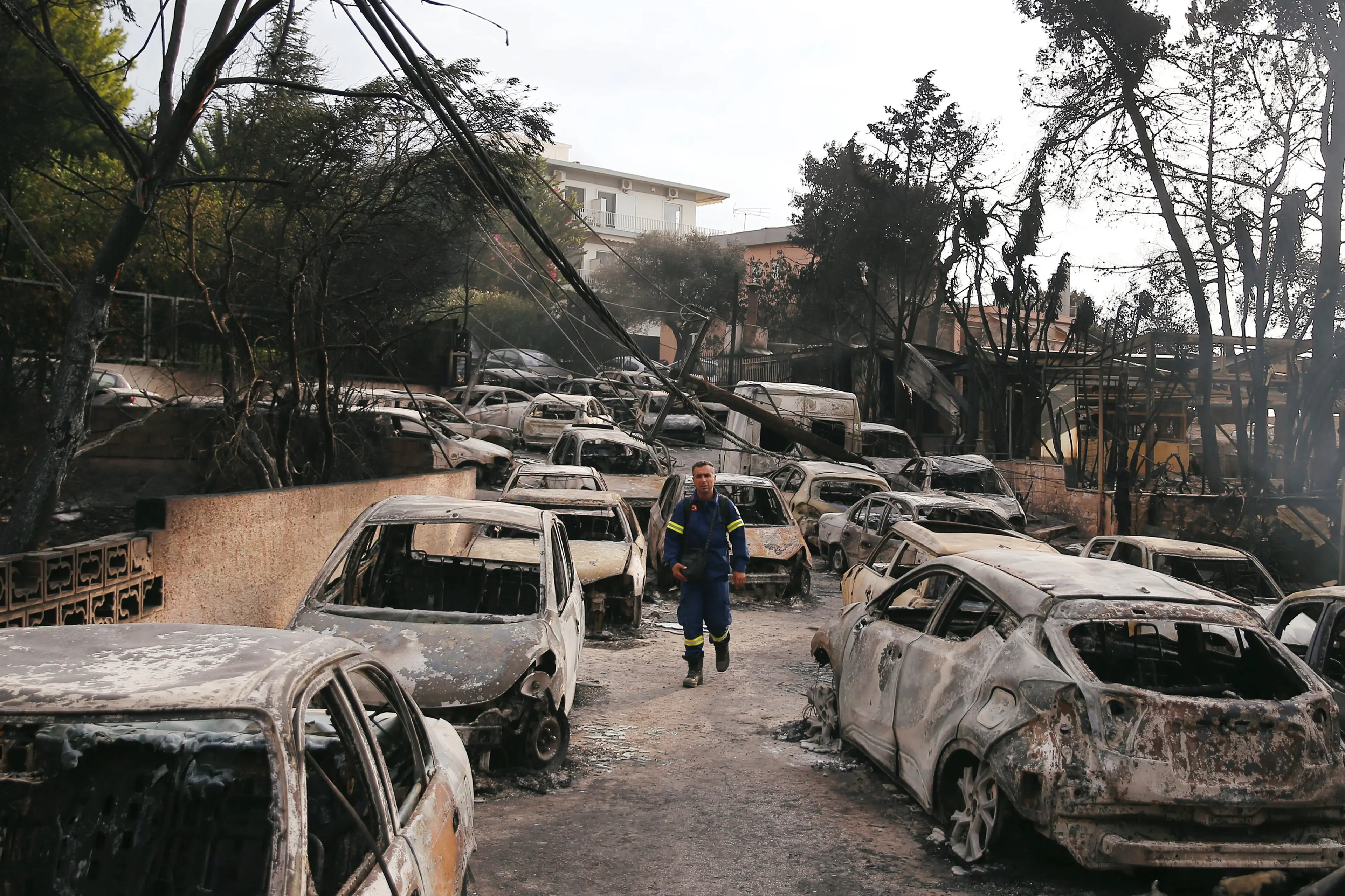 A firefighter walks among burned cars, following a wildfire at the village of Mati, near Athens