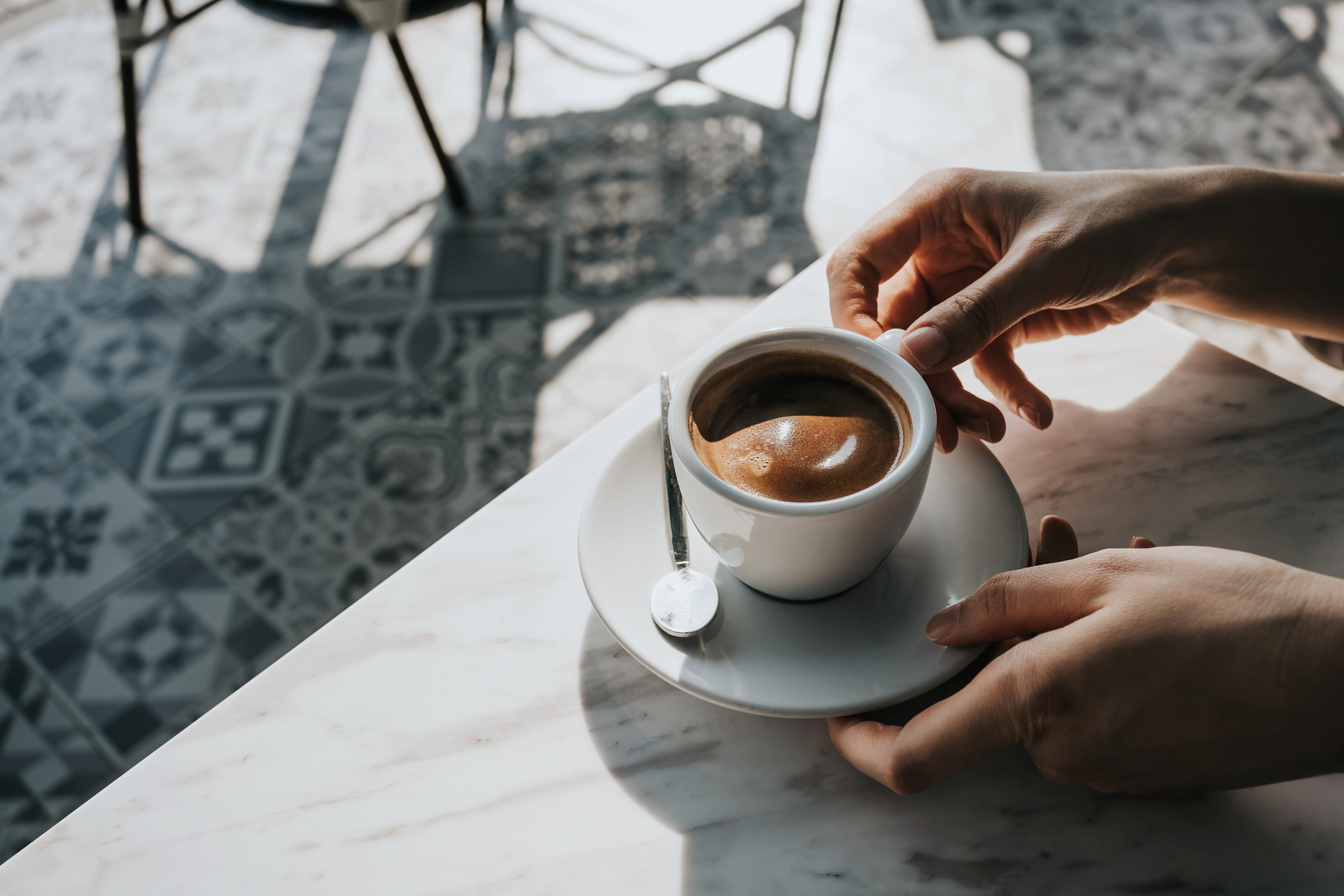 Close up of woman's hand holding a cup of coffee, drinking coffee in outdoor cafe against beautiful sunlight, having a relaxing moment. Enjoying life's simple pleasures