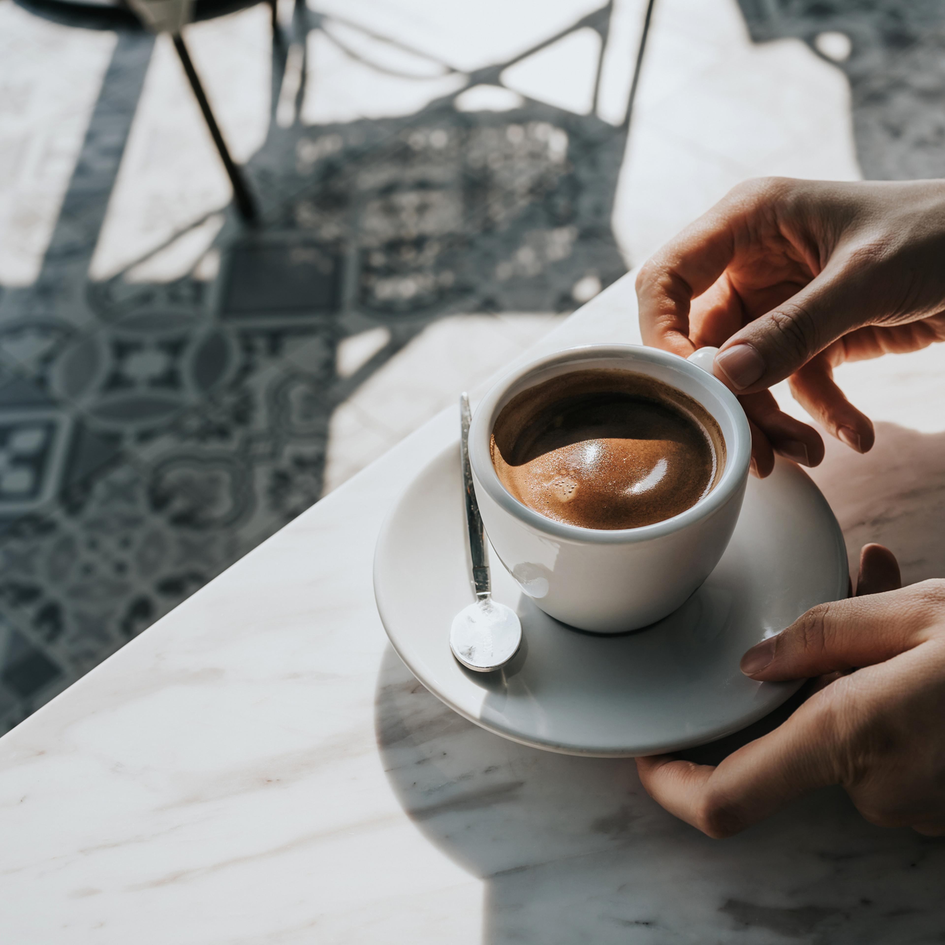 Close up of woman's hand holding a cup of coffee, drinking coffee in outdoor cafe against beautiful sunlight, having a relaxing moment. Enjoying life's simple pleasures
