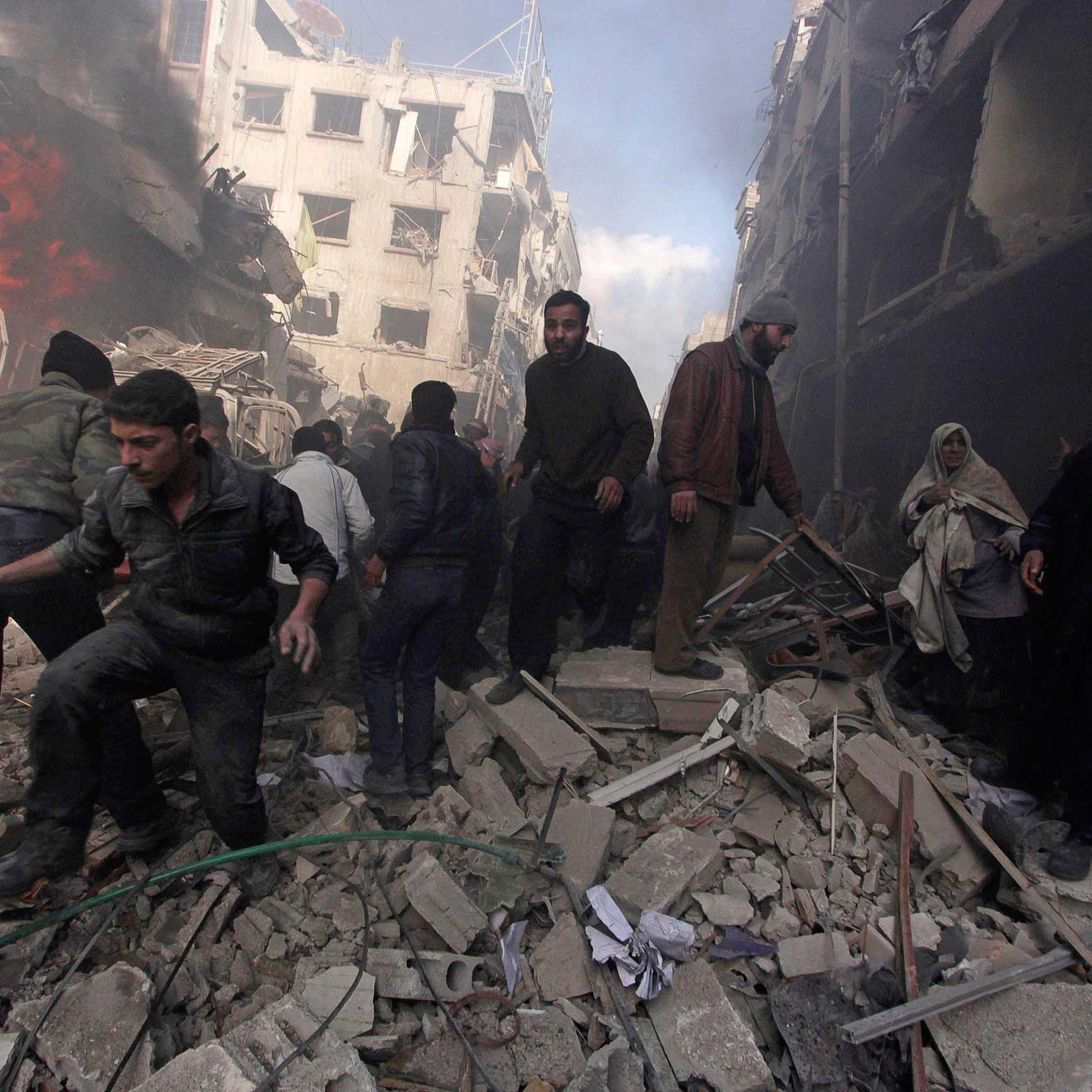 People walk on rubble as others try to put out a fire after what activists said were airstrikes followed by shelling by forces loyal to Syria's President Bashar Assad in the Douma neighborhood of Damascus, Feb. 9, 2015.