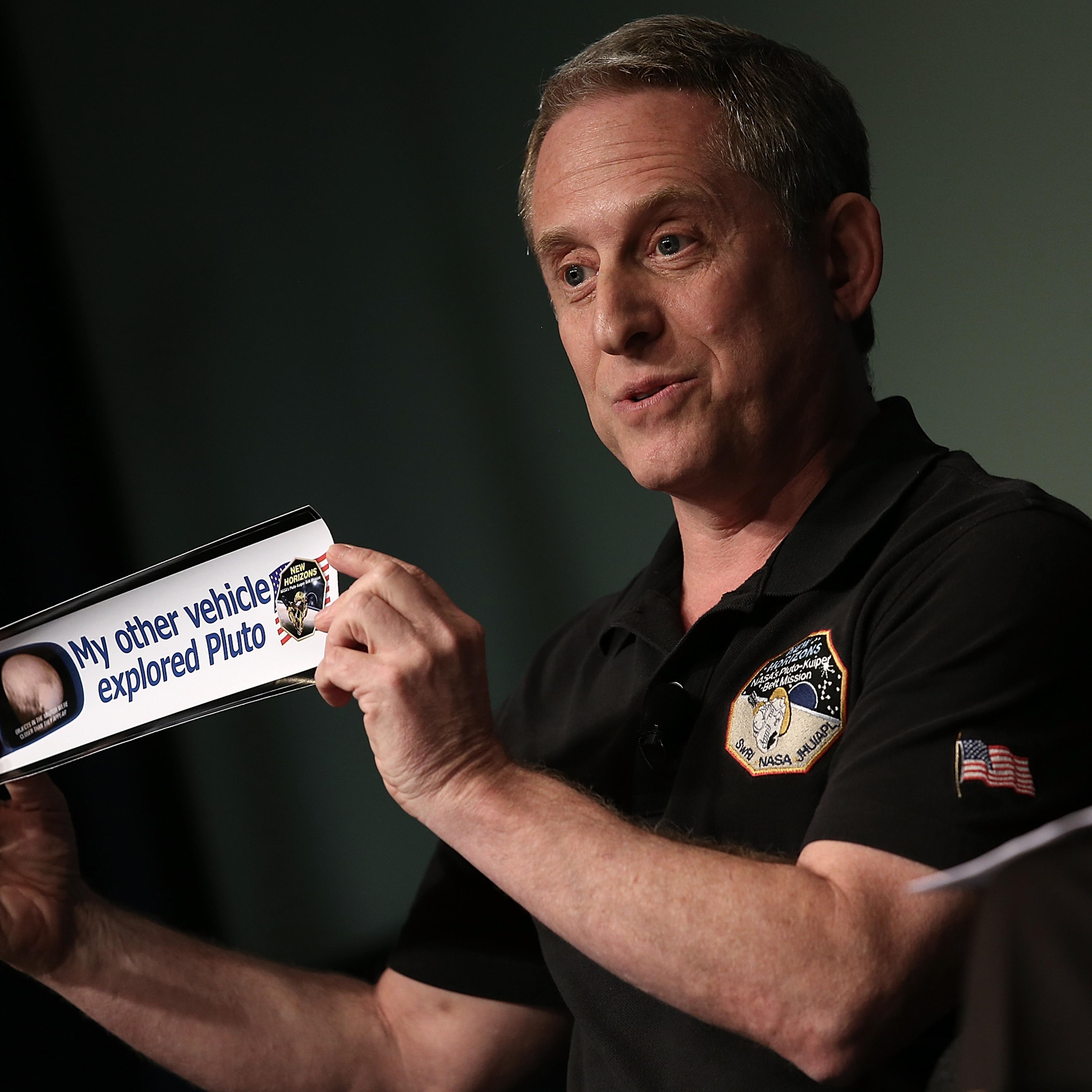 Alan Stern, principal investigator of NASA's New Horizons mission team, holds up a bumper sticker while delivering remarks during a press briefing at NASA headquarters in Washington, DC on July 24, 2015.