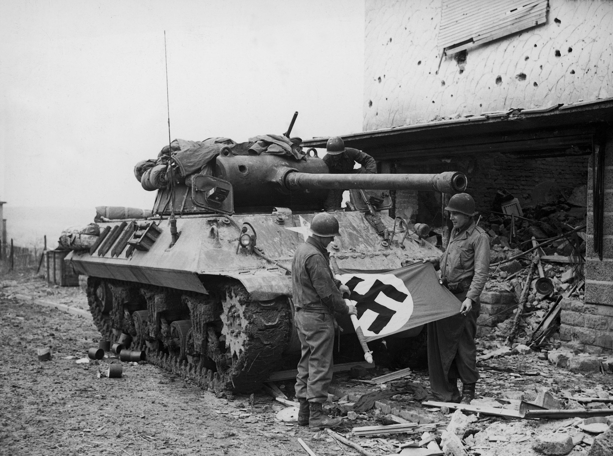 American soldiers of Patton's Third Army roll up a Nazi flag they have taken as a trophy after the capture of Bitburg, February 1945.