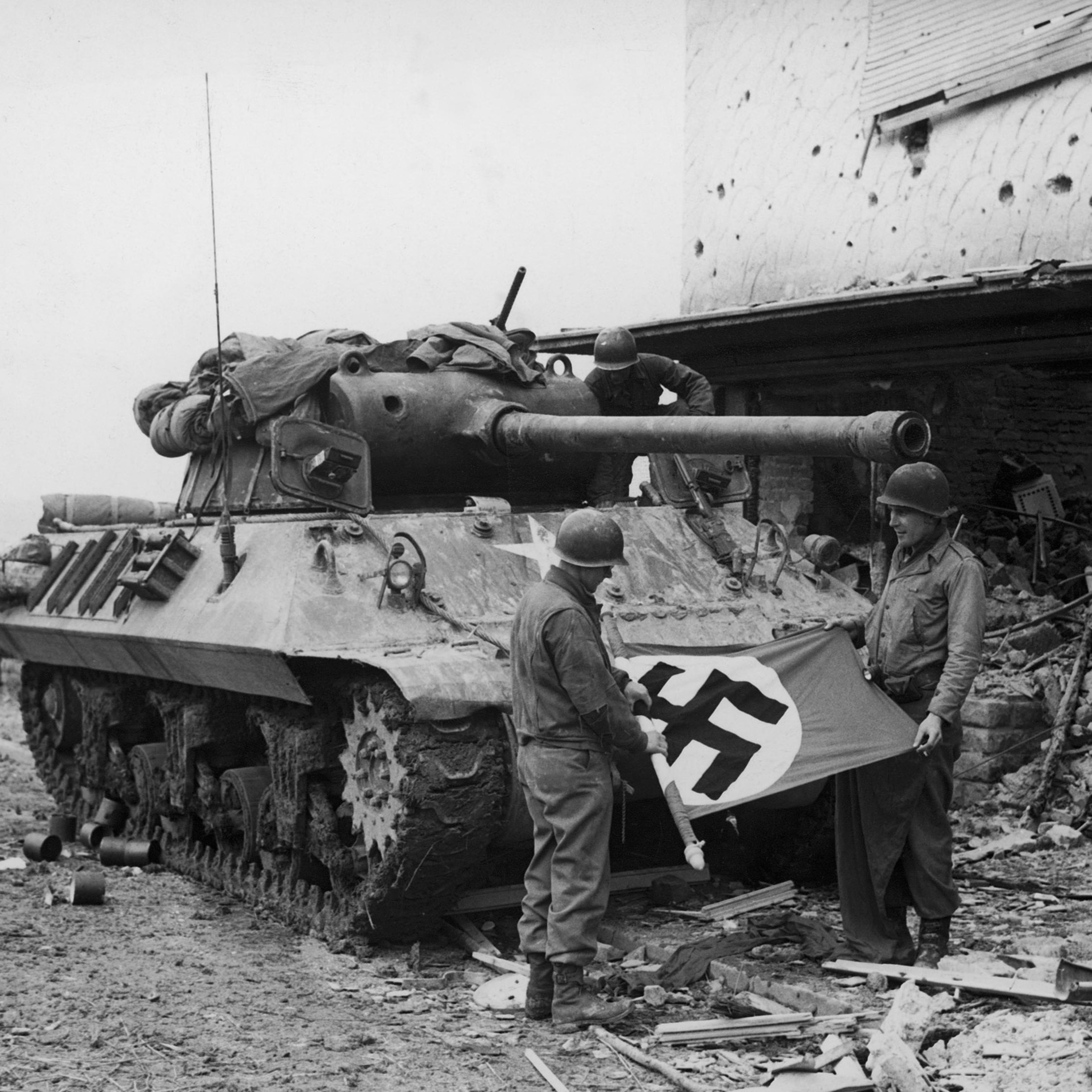 American soldiers of Patton's Third Army roll up a Nazi flag they have taken as a trophy after the capture of Bitburg, February 1945.