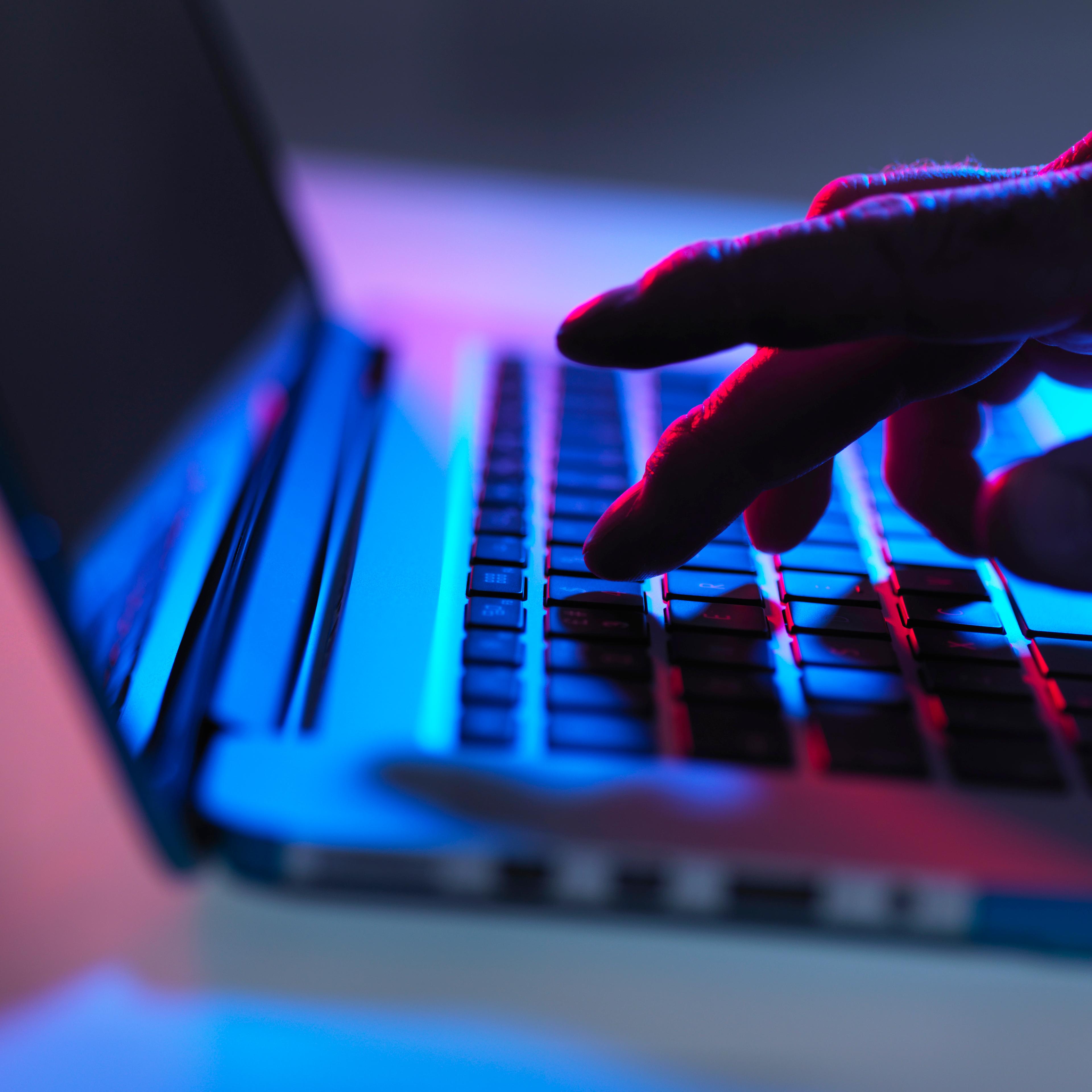 Silhouette of male hand typing on laptop keyboard at night
