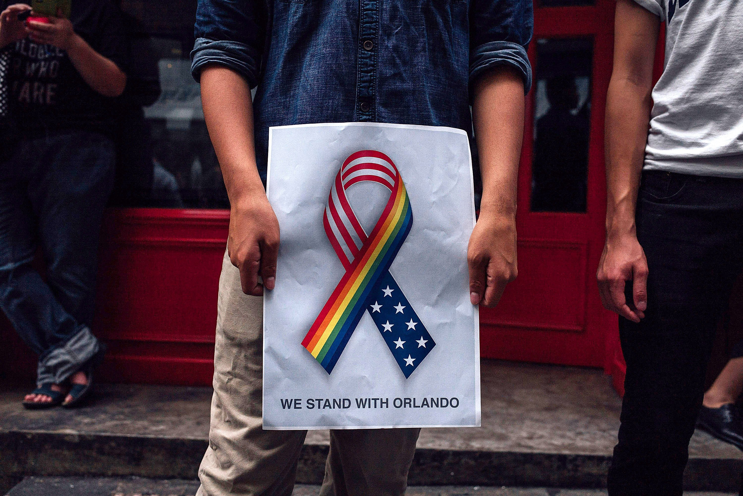 HONG KONG - JUNE 13: A man holds up a 'we stand together with Orlando' poster as people take part in a candlelight vigil for the victims of a shooting in a gay nightclub in Orlando, Florida on June 13, 2016 in Hong Kong, Hong Kong. The vigil is put toget
