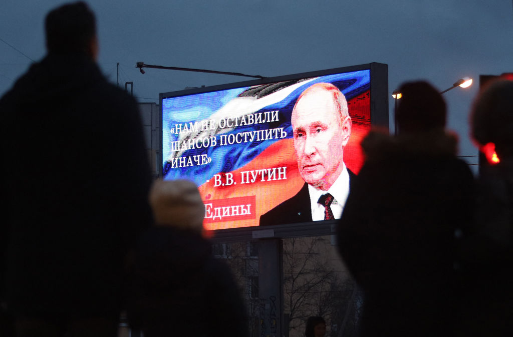 Bystanders gather in front of a board displaying an image of Russian President Vladimir Putin