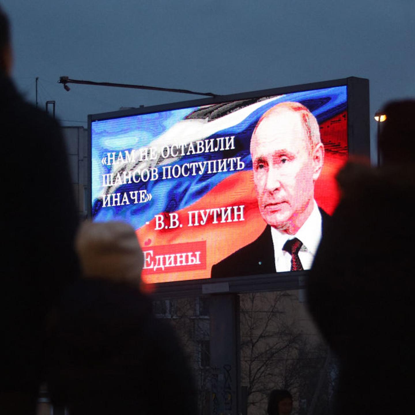 Bystanders gather in front of a board displaying an image of Russian President Vladimir Putin
