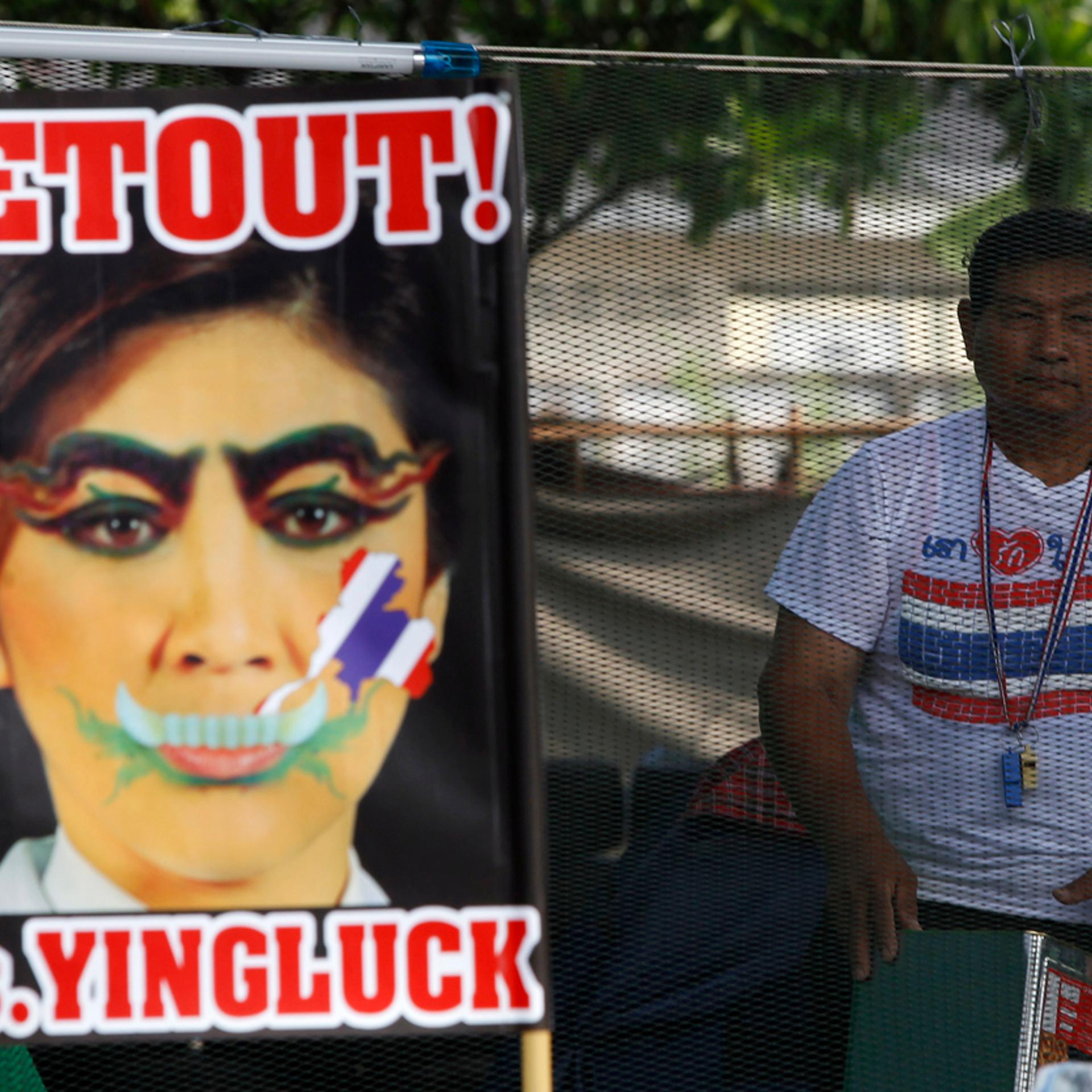 An anti-government protester stands next to a defaced image of Thailand's PM Yingluck during a rally in Bangkok