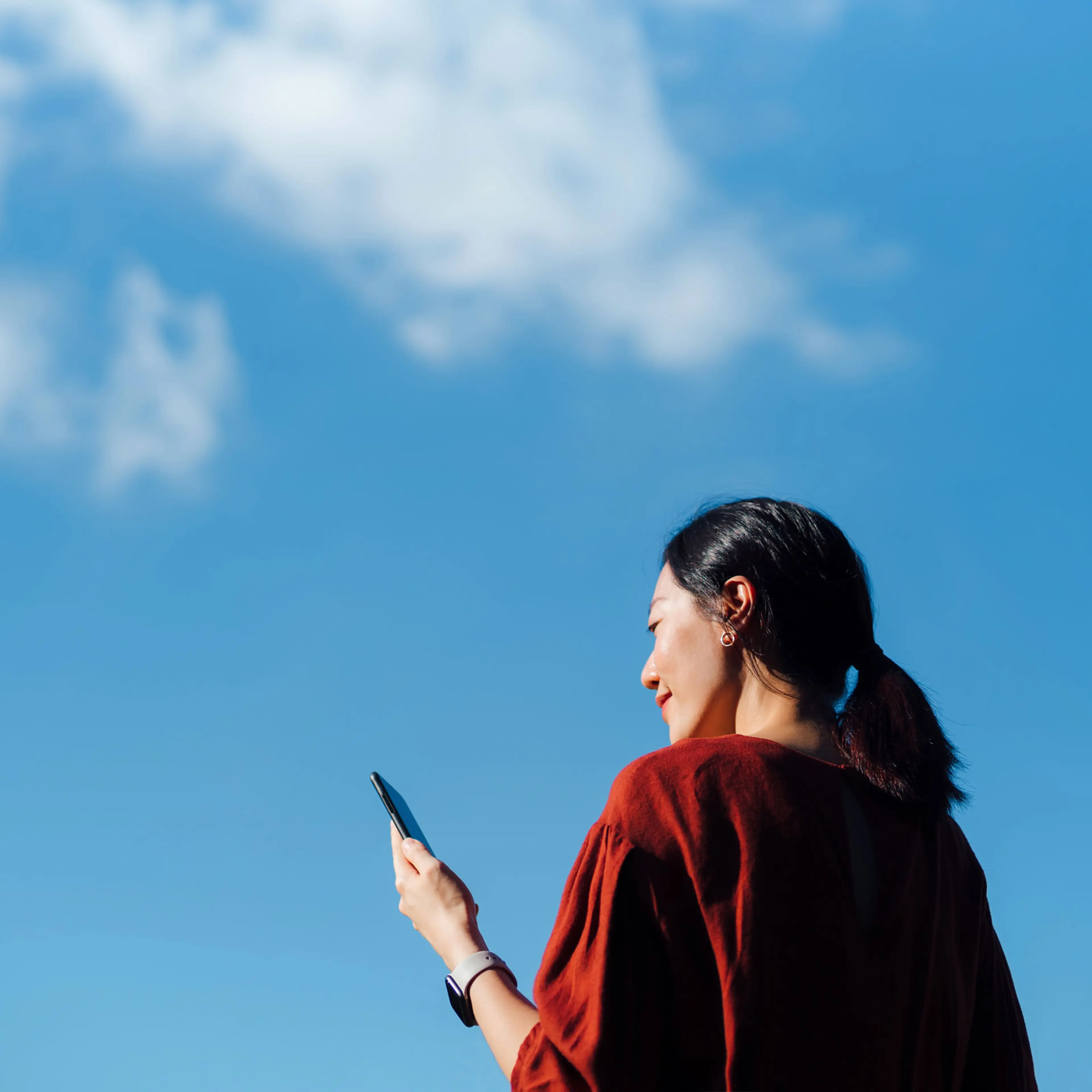 Low angle portrait of young woman using smartphone against blue sky