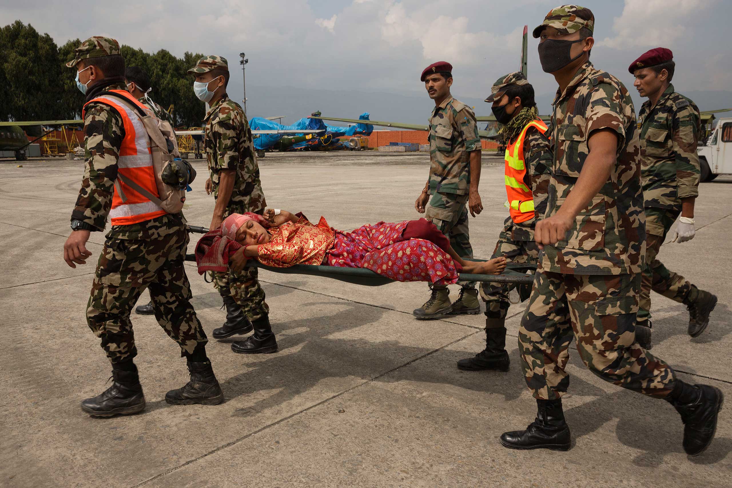 Nepal earthquake. Small village in foothills with people gathering near helipad to watch Nepal Army helicopter land with supplies. Cremation pyres in Katmandu at Pashupatinath Temple on Bagmati River.by James Nachtwey
