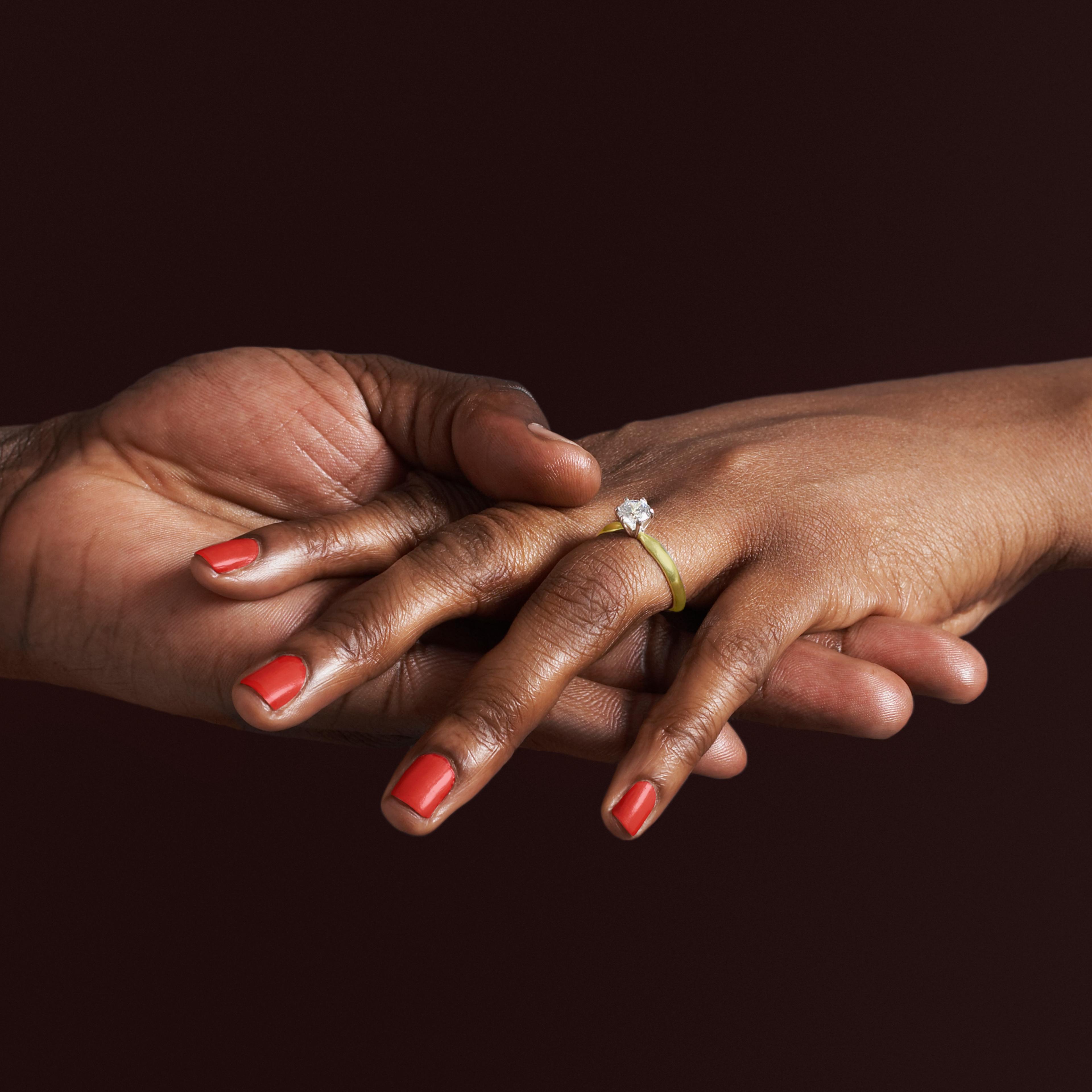 African woman with engagement ring holding fiancee's hand