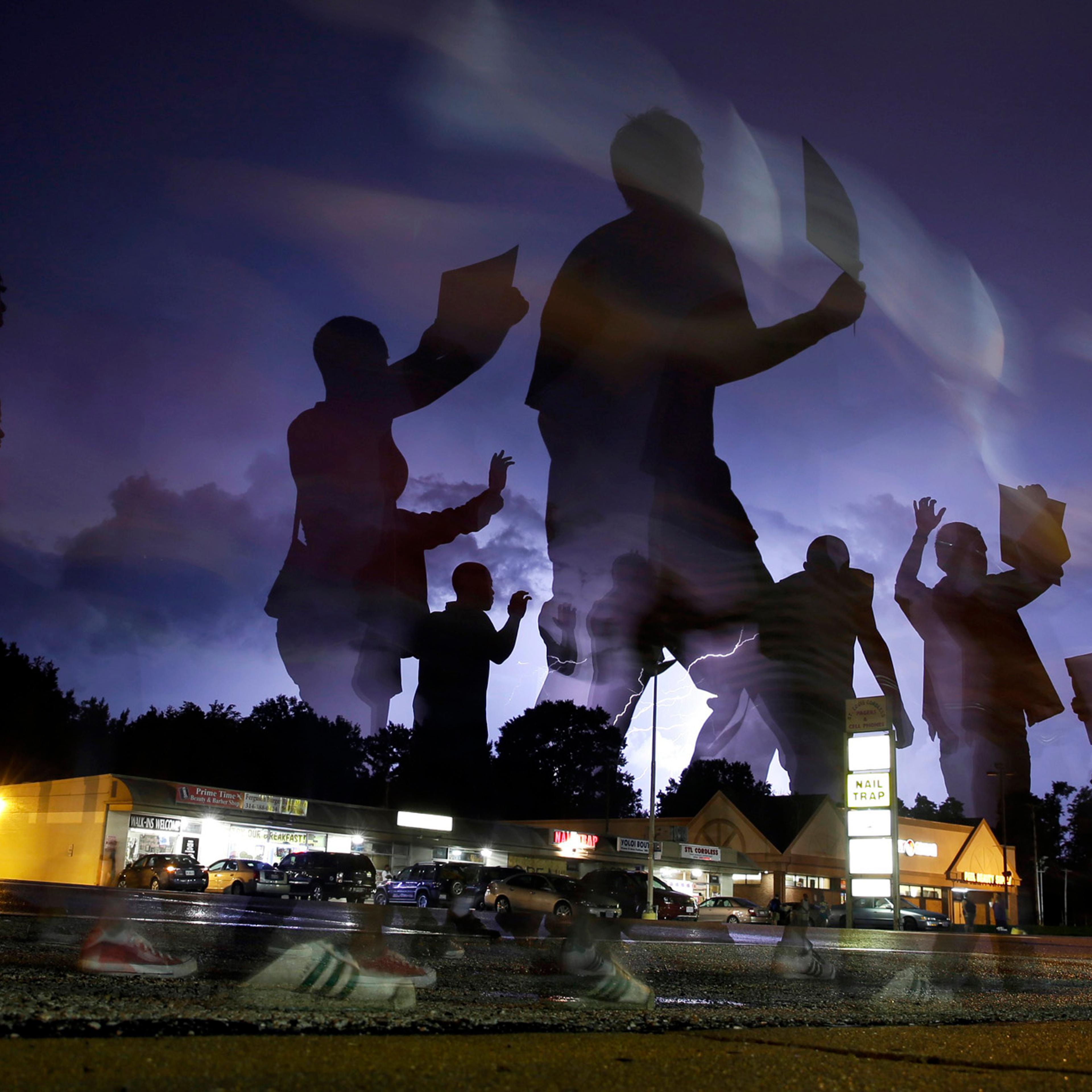 Protesters march in the street as lightning flashes in the distance in Ferguson, Mo, Aug. 20, 2014.