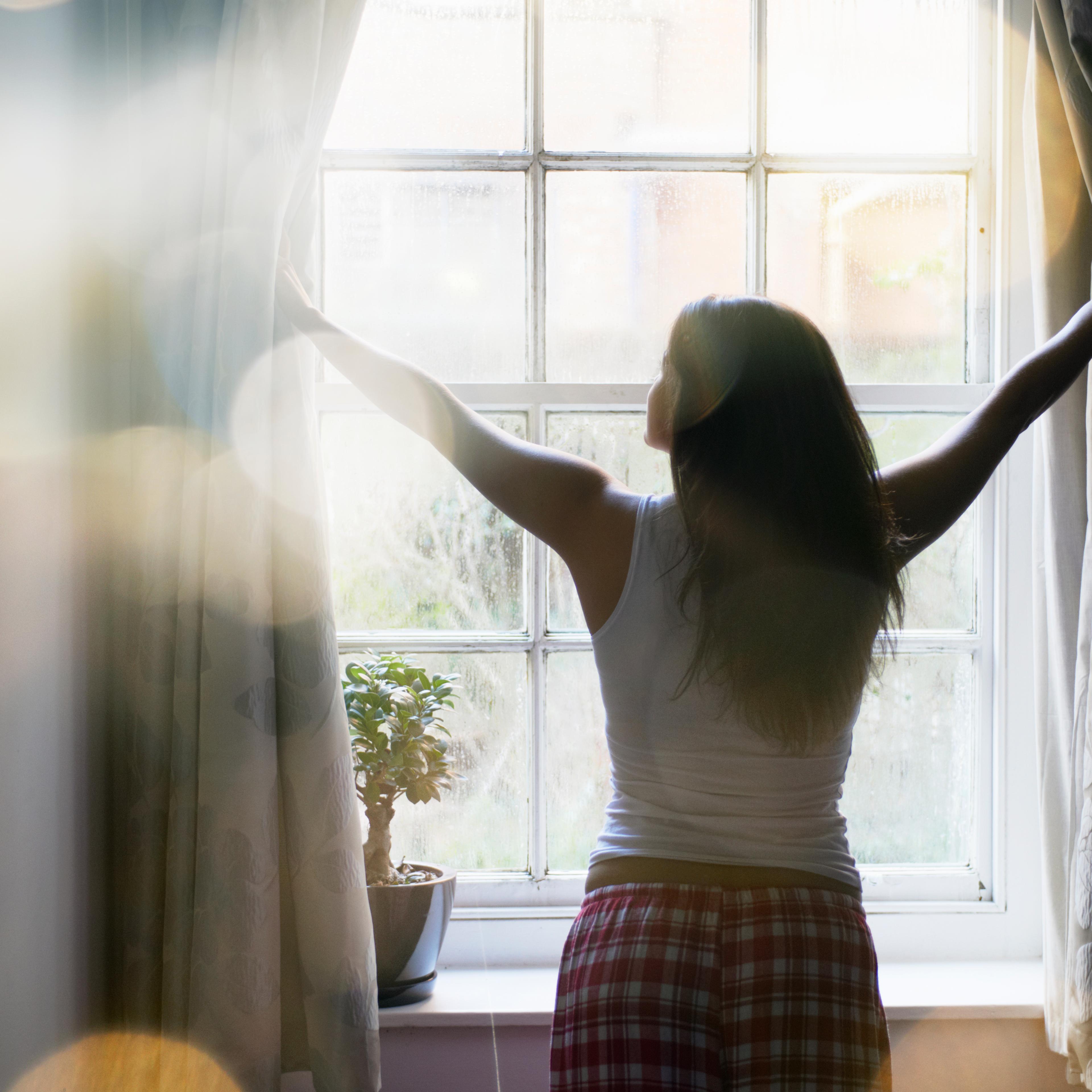 woman opening curtains in the morning