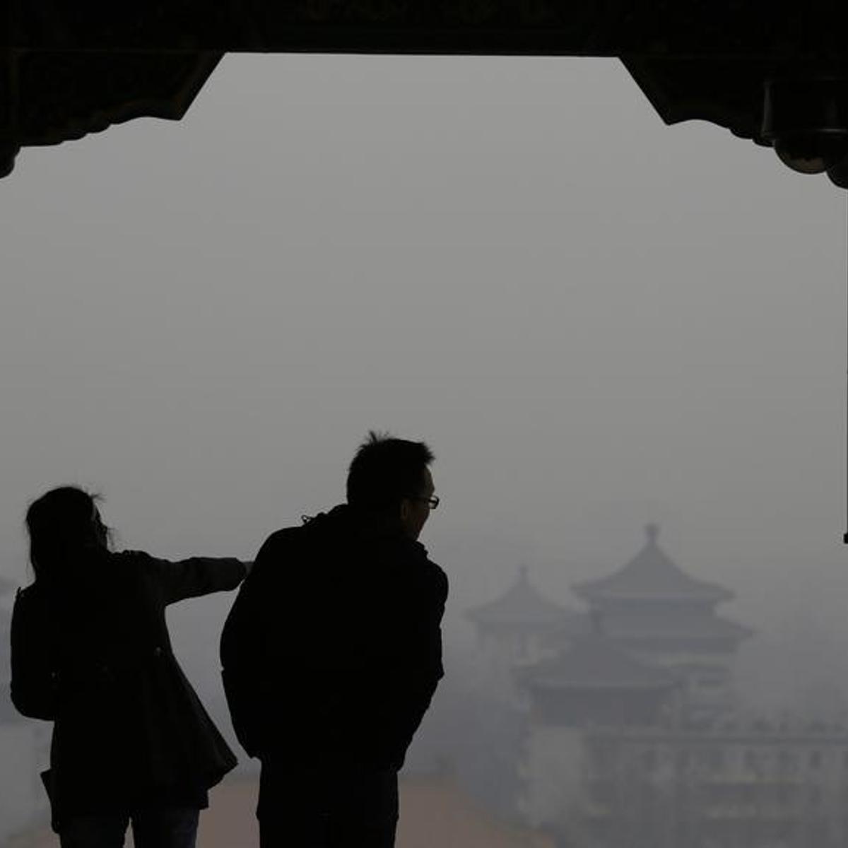 Visitors are silhouetted against thick smog on the top of Jingshan Park near the Forbidden City in Beijing