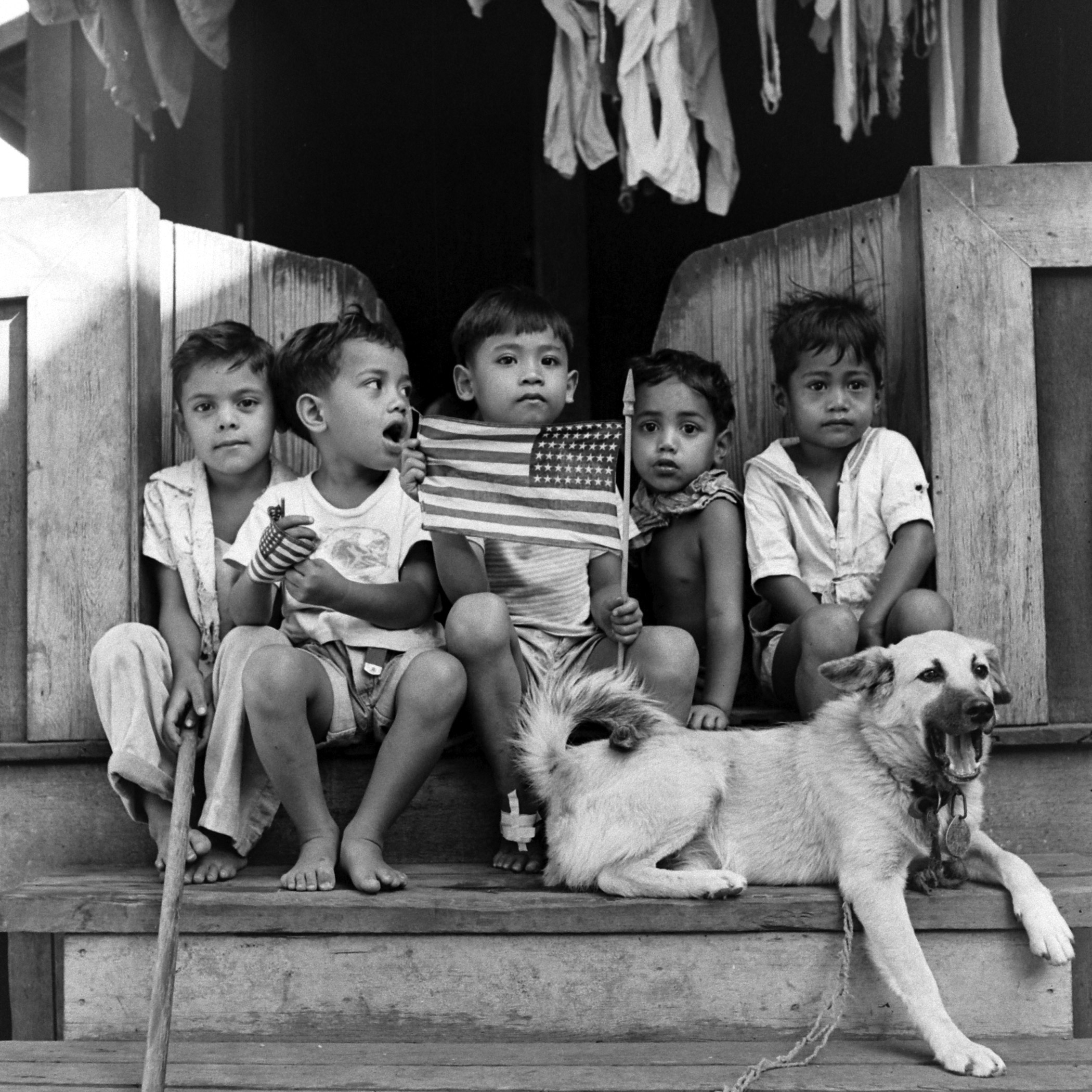 Children with American flag hanging out on a front porch.