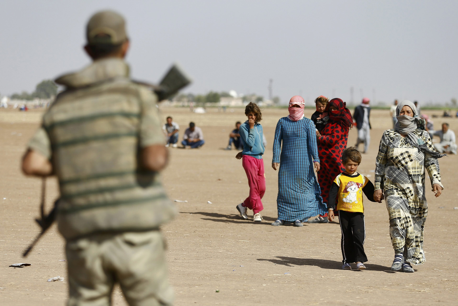 A Turkish soldier watches as Kurdish Syrian refugees walk on the Turkish-Syrian border near the southeastern town of Suruc in Sanliurfa province, Sept. 24, 2014.