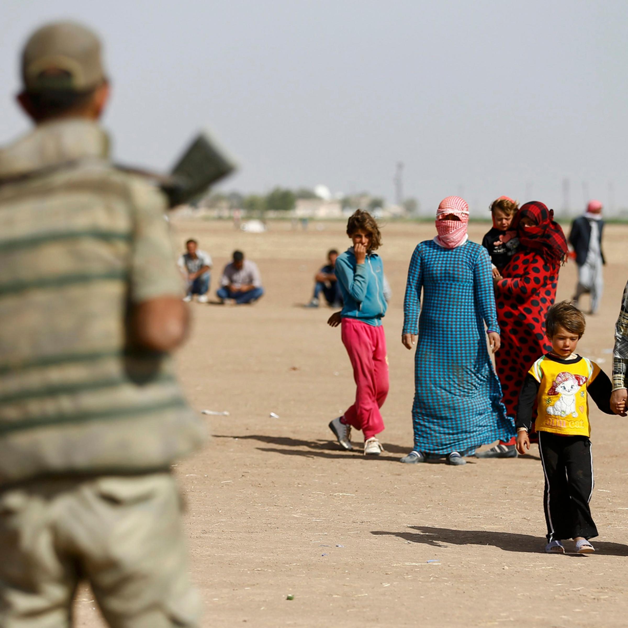 A Turkish soldier watches as Kurdish Syrian refugees walk on the Turkish-Syrian border near the southeastern town of Suruc in Sanliurfa province, Sept. 24, 2014.