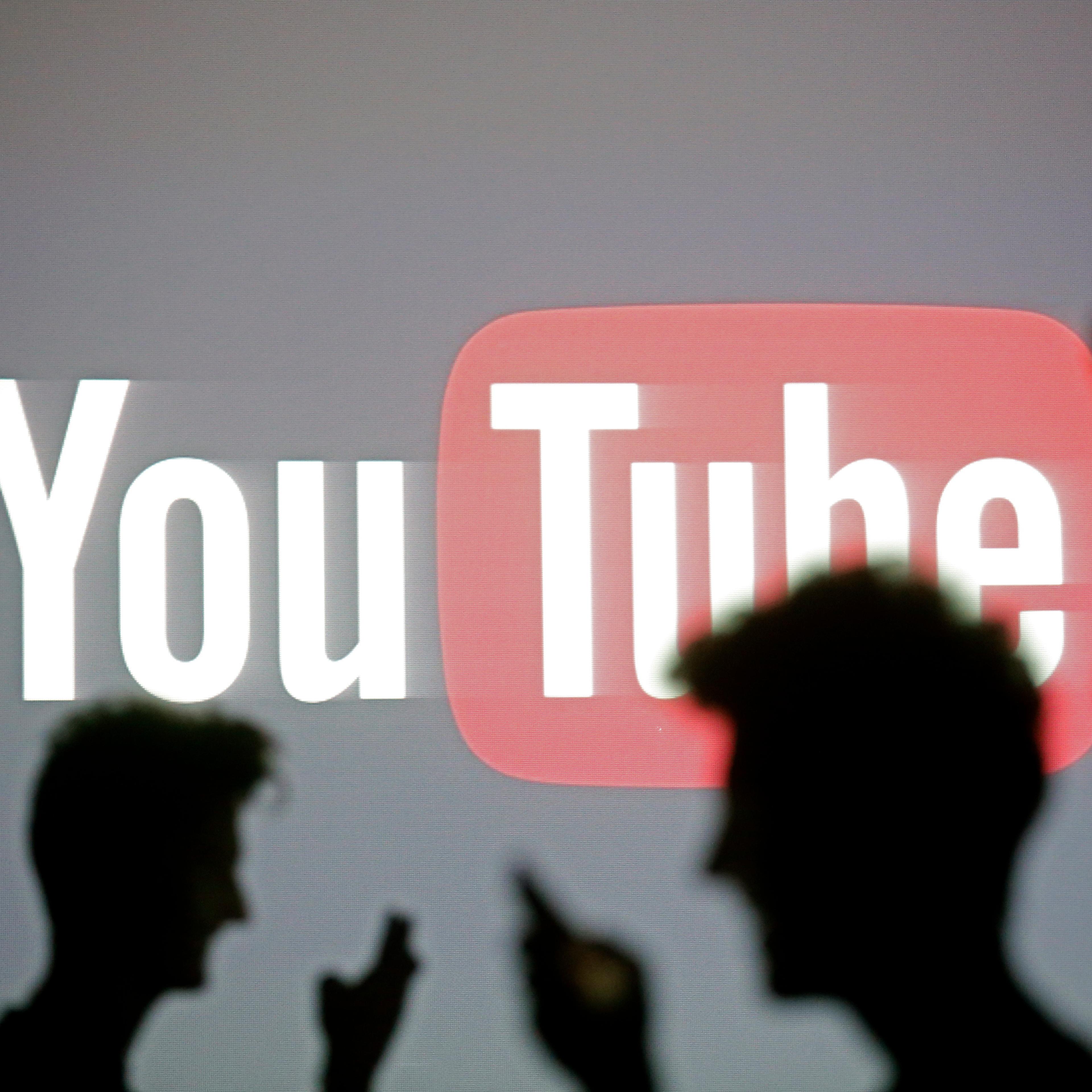 People pose with mobile devices in front of projection of Youtube logo in this picture illustration taken in Zenica