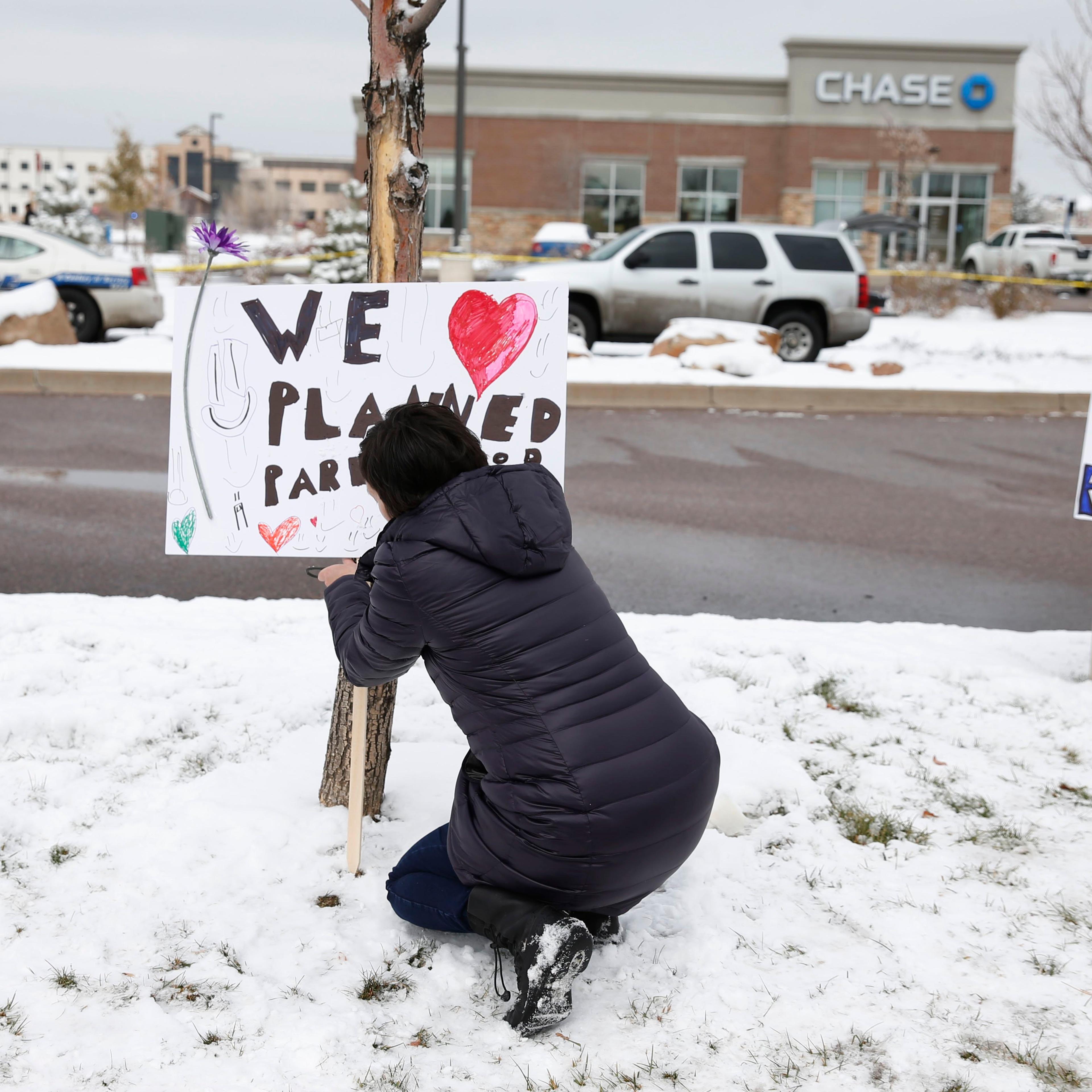 Bethany Winder, a nurse who lives in Colorado Springs, Colo., plants a sign in support of Planned Parenthood just south of its clinic as police investigators gather evidence near the scene of Friday's shooting at the clinic on Nov. 29, 2015.